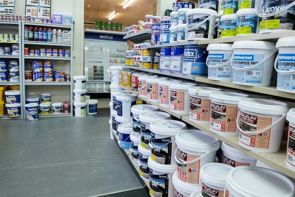 A well-stocked aisle in a hardware or paint store featuring shelves filled with various sizes of paint buckets and cans.