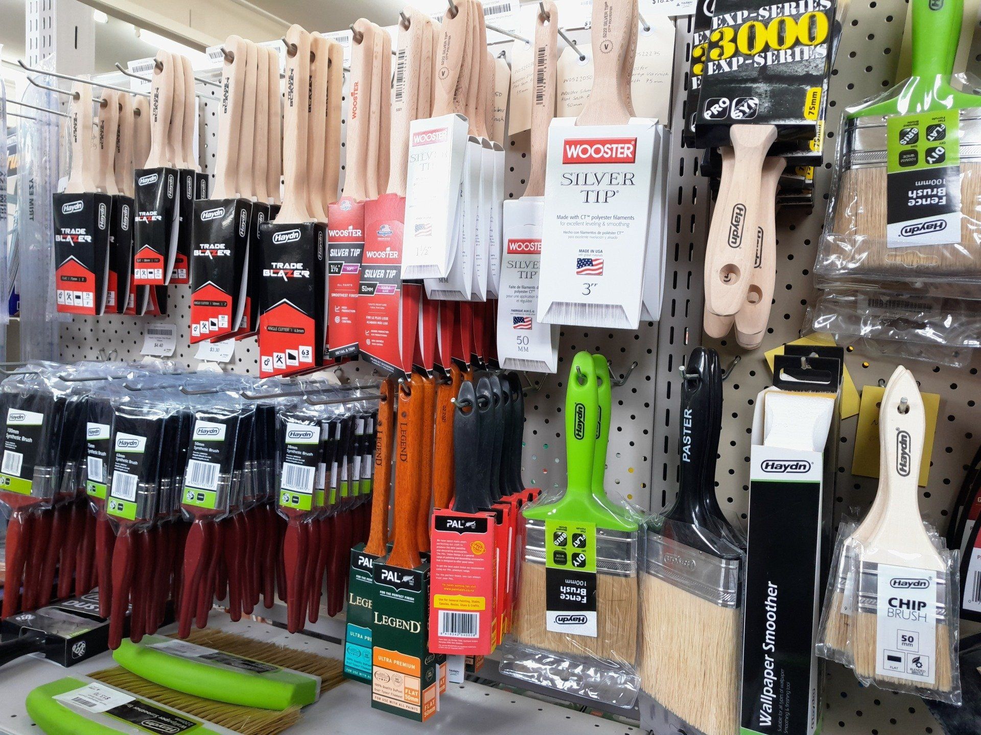 A display of assorted paintbrushes hanging on hooks in a store, including various widths, handle colors, and brands.
