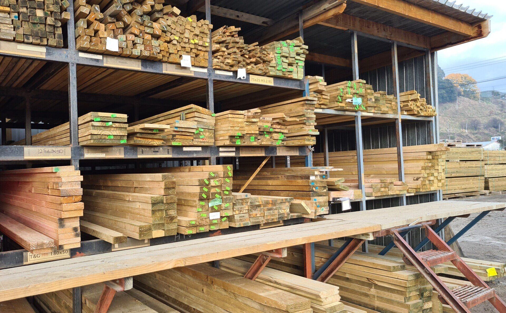 Lumber yard featuring metal shelving units stacked with various lengths and types of wooden planks and beams.