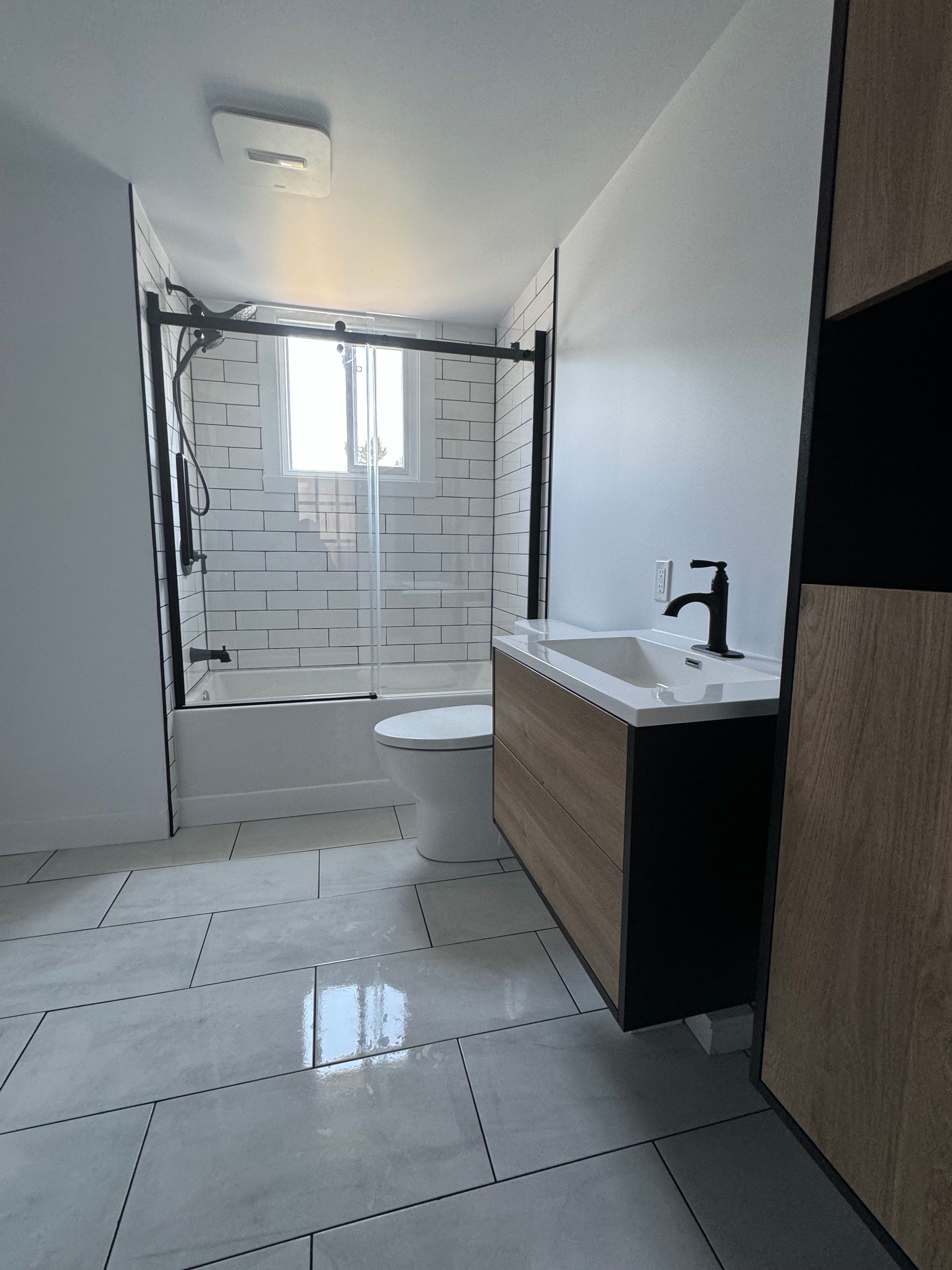 Salle de bains moderne avec des touches de blanc et de noir ; douche, meuble-lavabo et toilettes visibles.