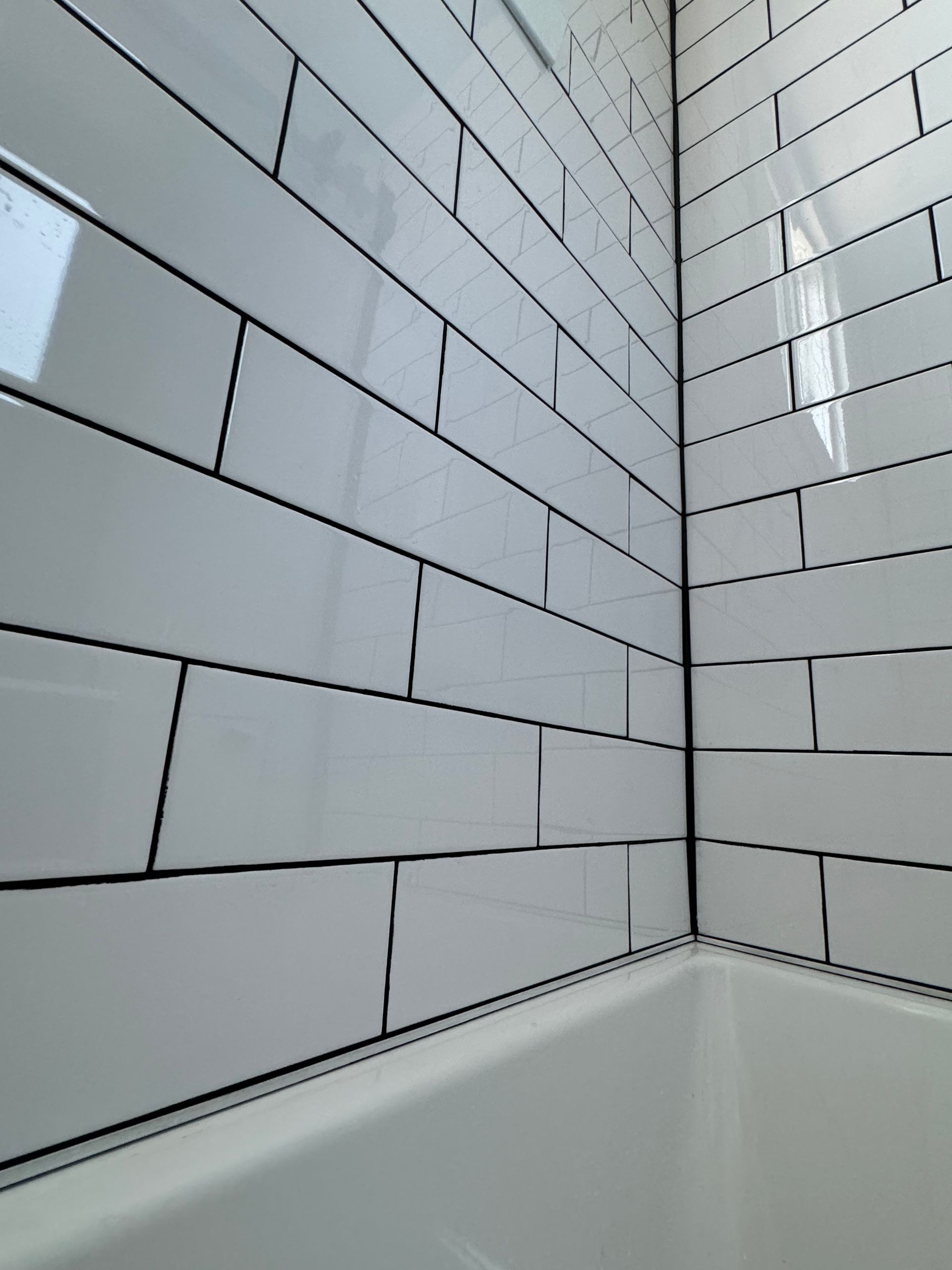 Carrelage métro blanc avec joints noirs dans un coin de salle de bains, à côté d'une baignoire blanche.