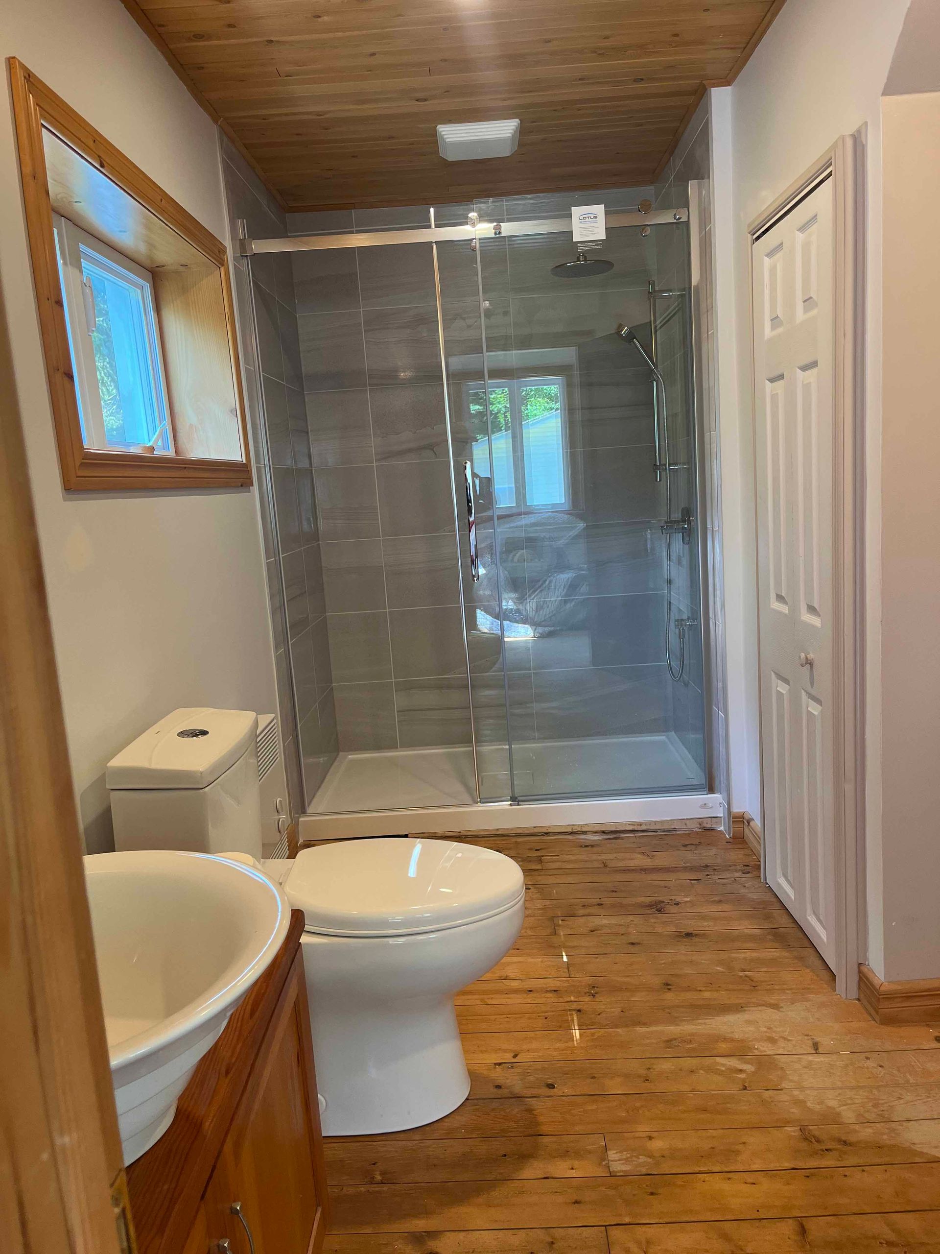 Salle de bains avec douche en verre, toilettes, lavabo, sol et plafond en bois.