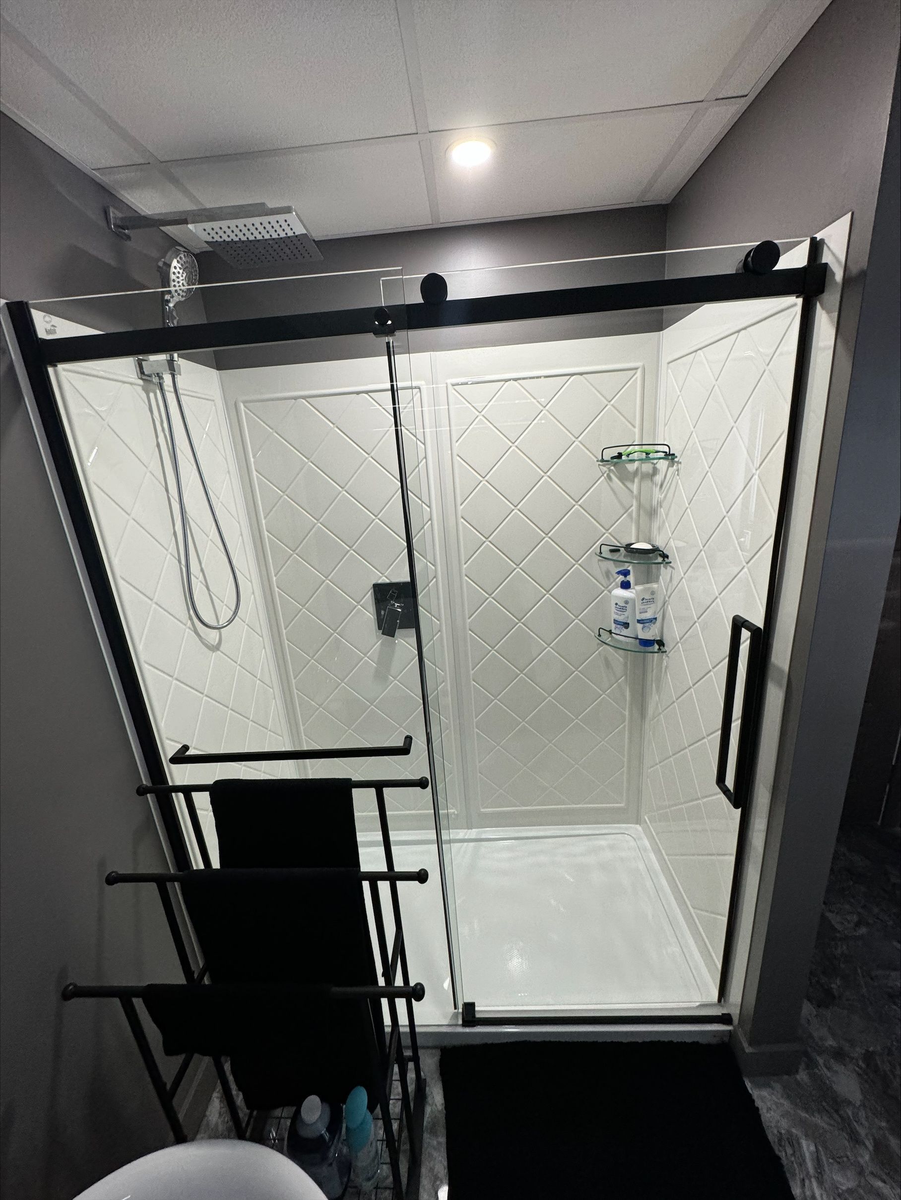 Une salle de bain avec une porte de douche coulissante en verre et un cadre noir.