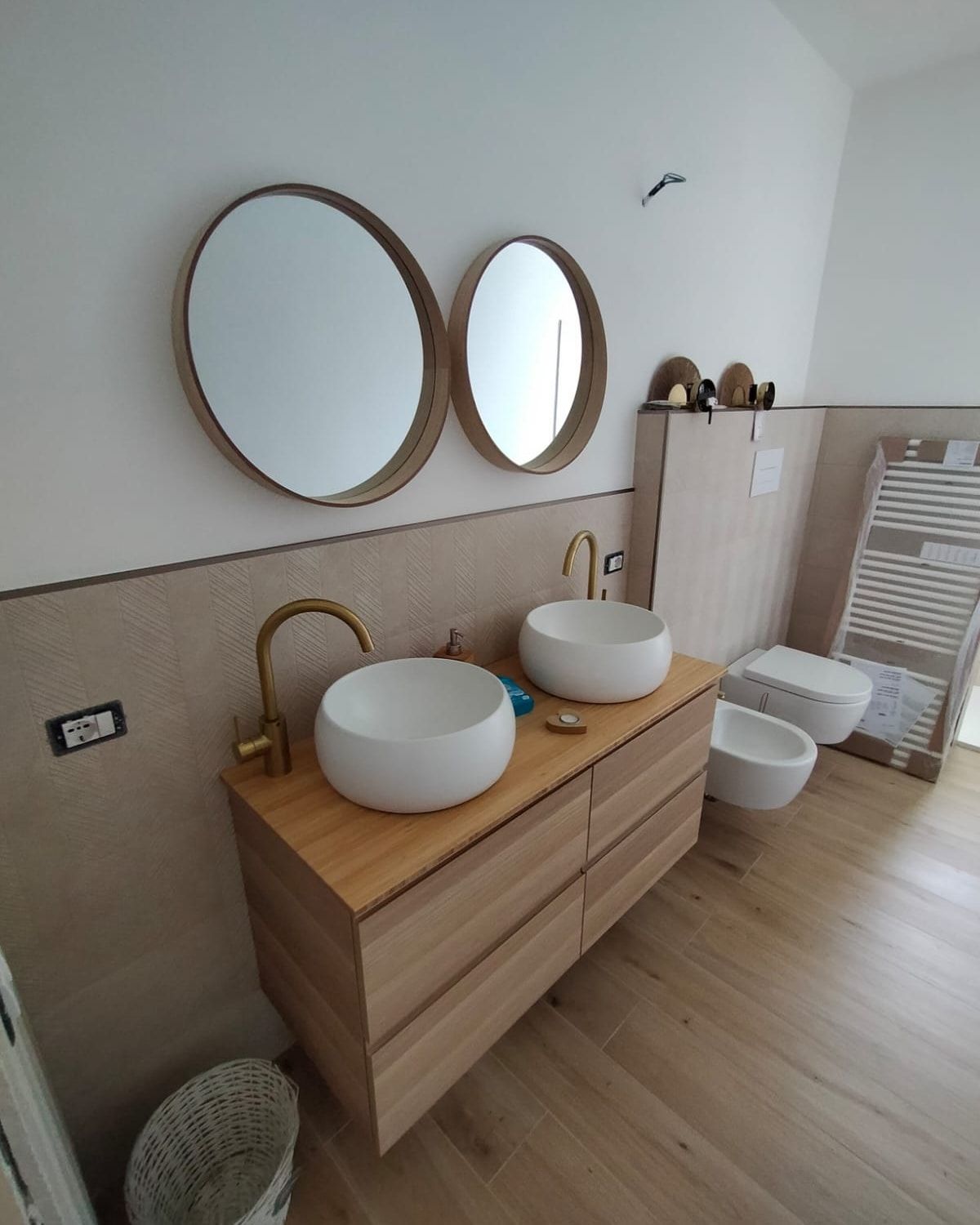 Bagno moderno con doppio lavabo a ciotola, specchi rotondi, mobiletto in legno e portasciugamani.