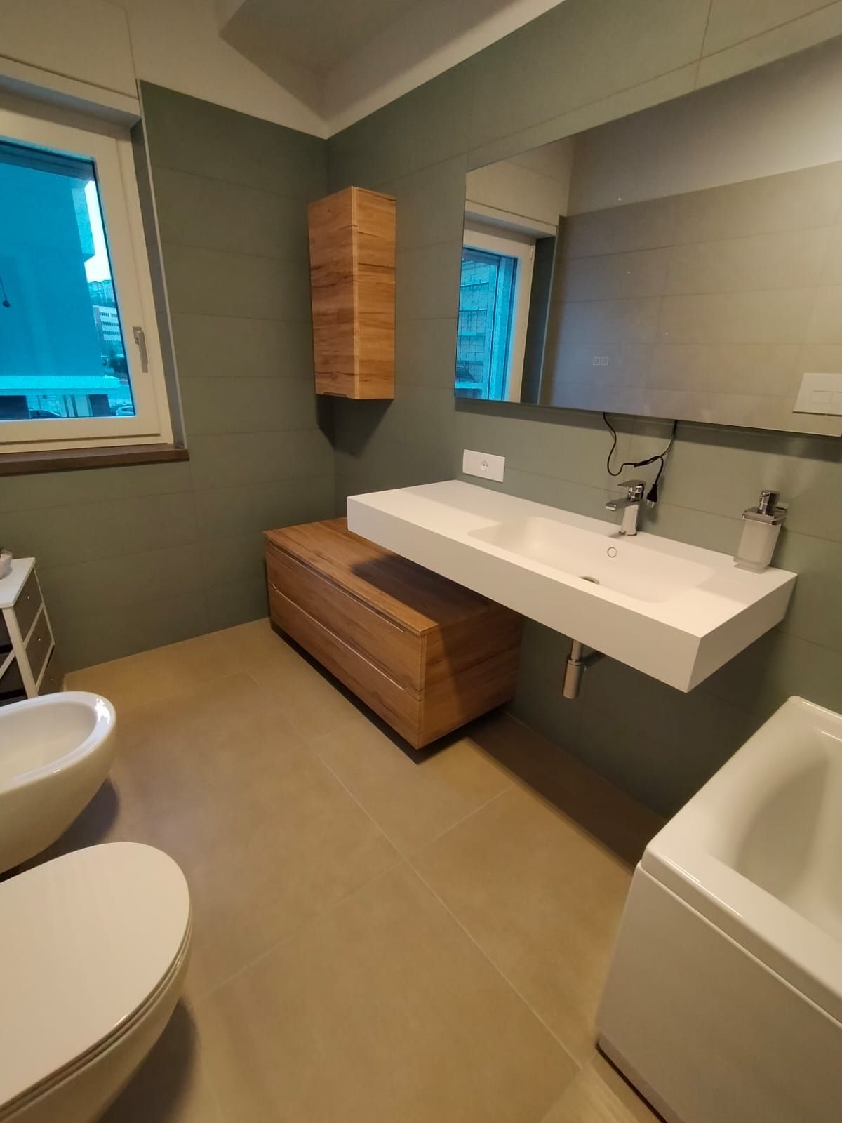 Bagno moderno con lavabo a parete, mobiletto sospeso in legno, vasca da bagno, WC e specchio.