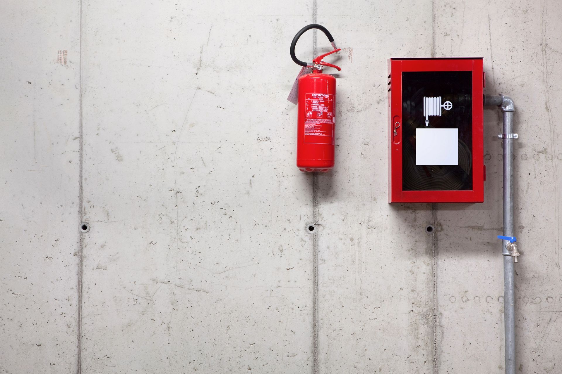 Estintore rosso e cassetta di allarme antincendio montati su un muro di cemento grigio.