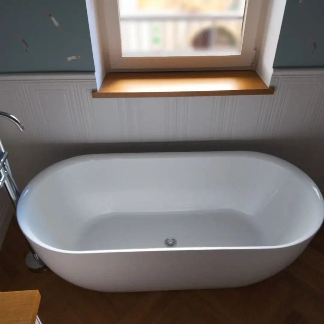 Vasca da bagno bianca freestanding posizionata sotto una finestra in un bagno