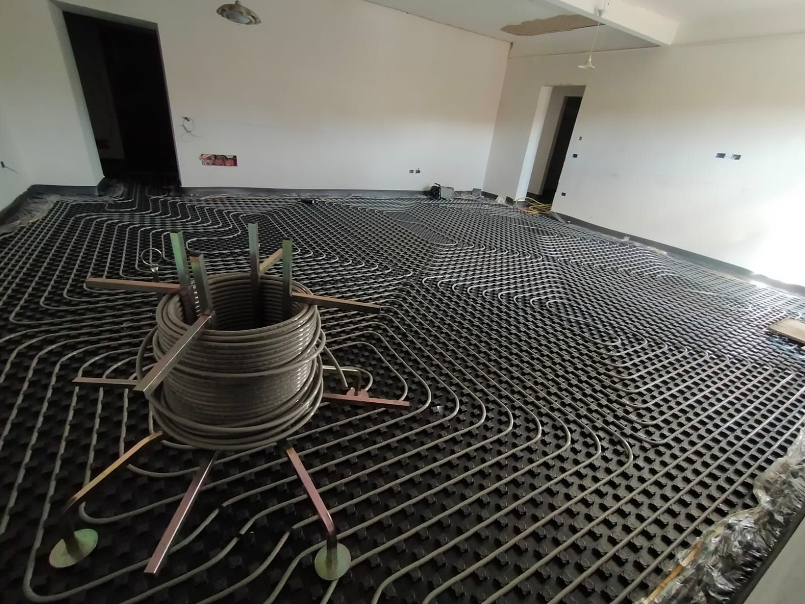 Interno di una stanza in costruzione con una griglia di tubi metallici sul pavimento e una spirale di tubo flessibile al centro.