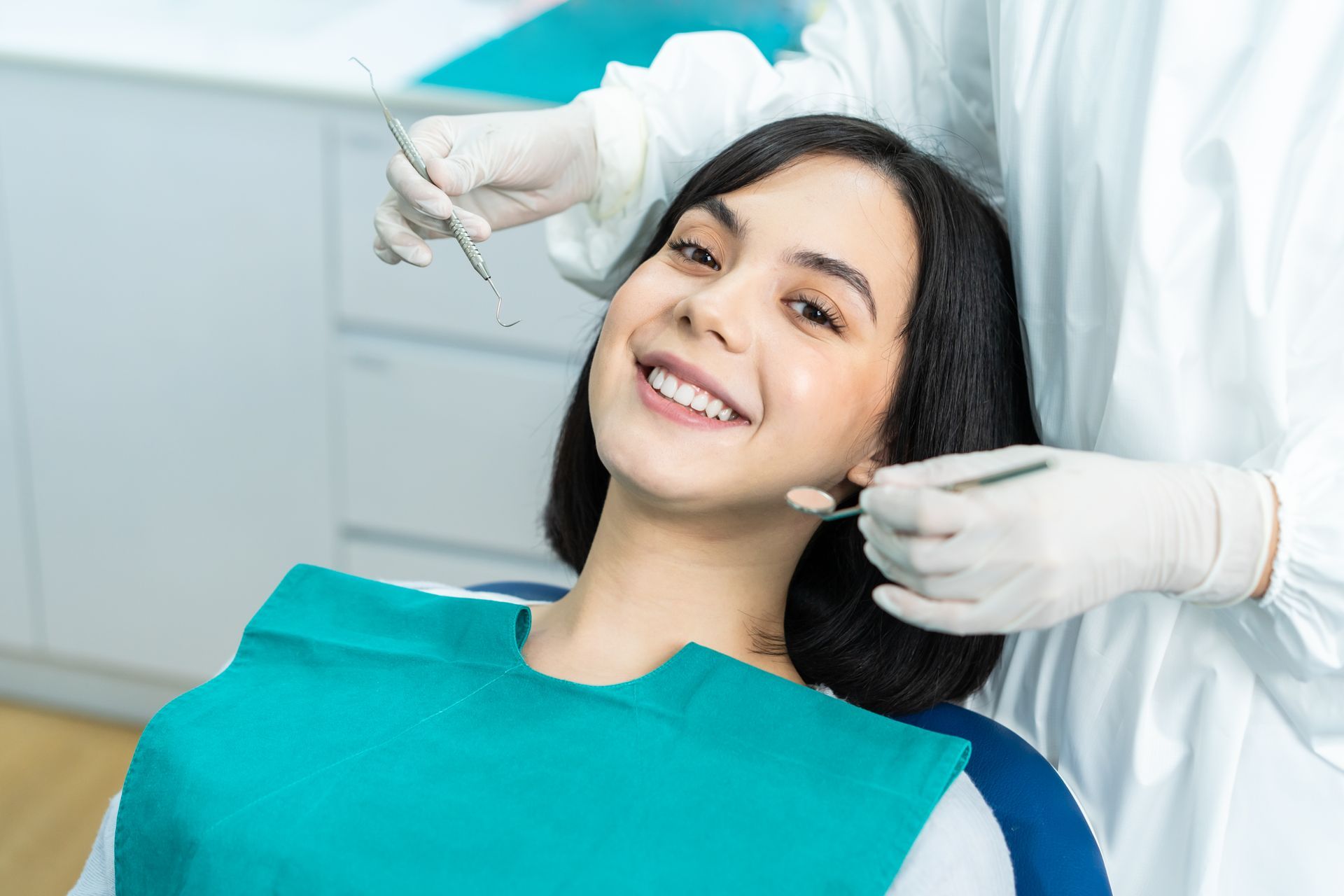 Une femme sur une chaise dentaire sourit pendant que le dentiste examine ses dents.
