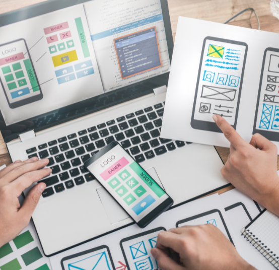A team of designers collaborates on a mobile app interface, using sketches, a smartphone, and a laptop to create wireframes.