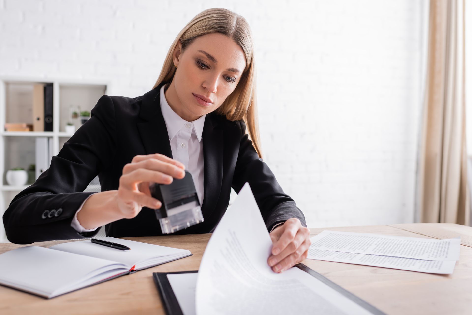 Woman in black suit stamping a document at a desk in an office.