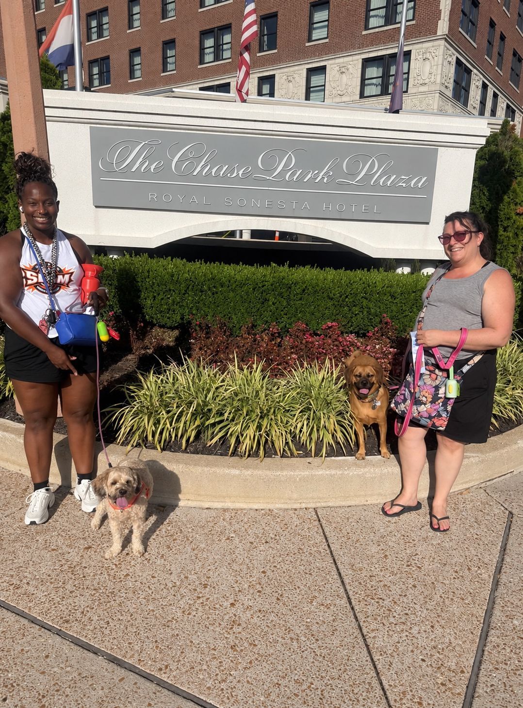 Two women standing with a dog in front of The Charles on the Plaza sign