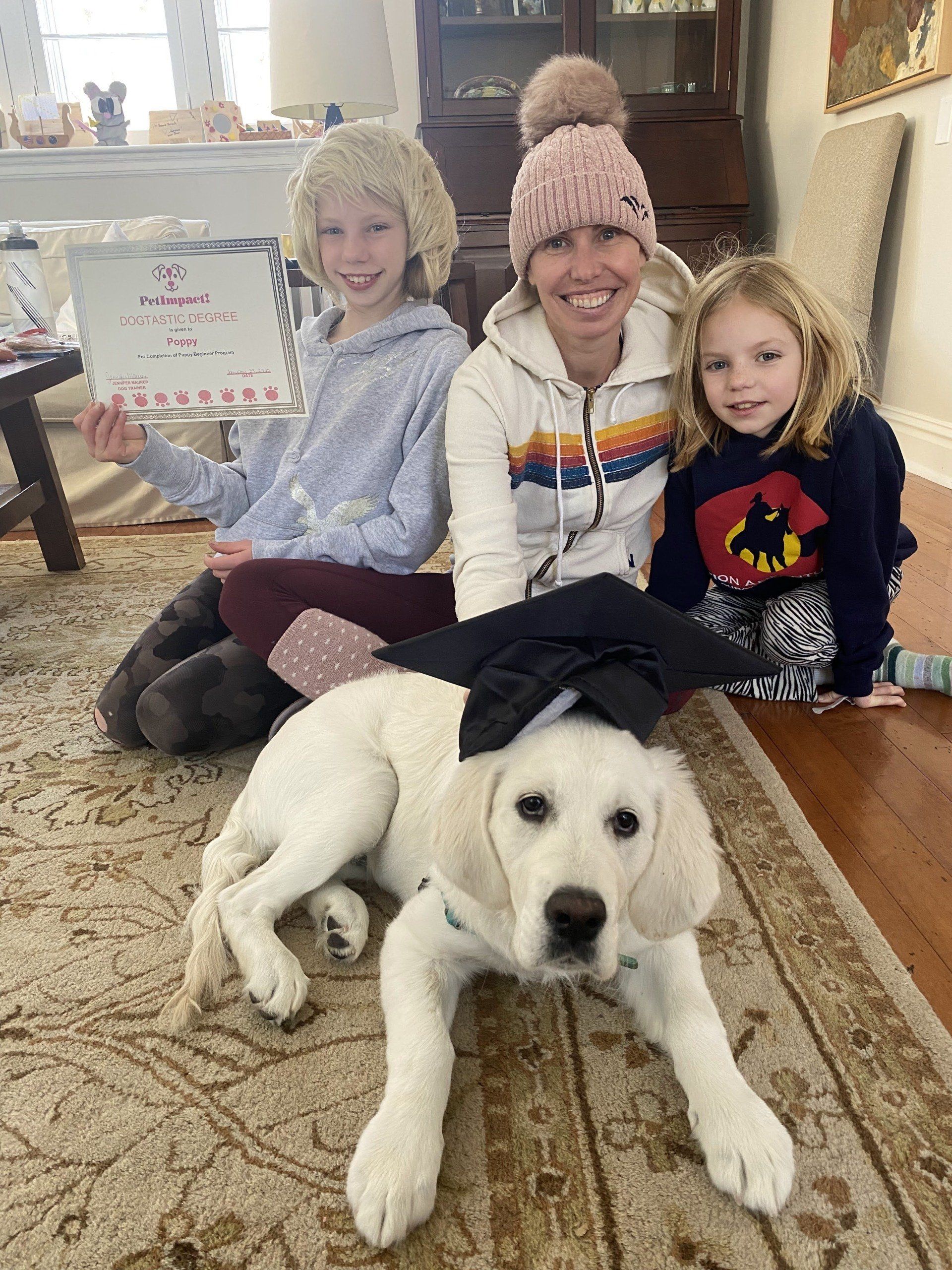 Family with a golden retriever puppy; sitting on a rug indoors. Woman and two children smile.