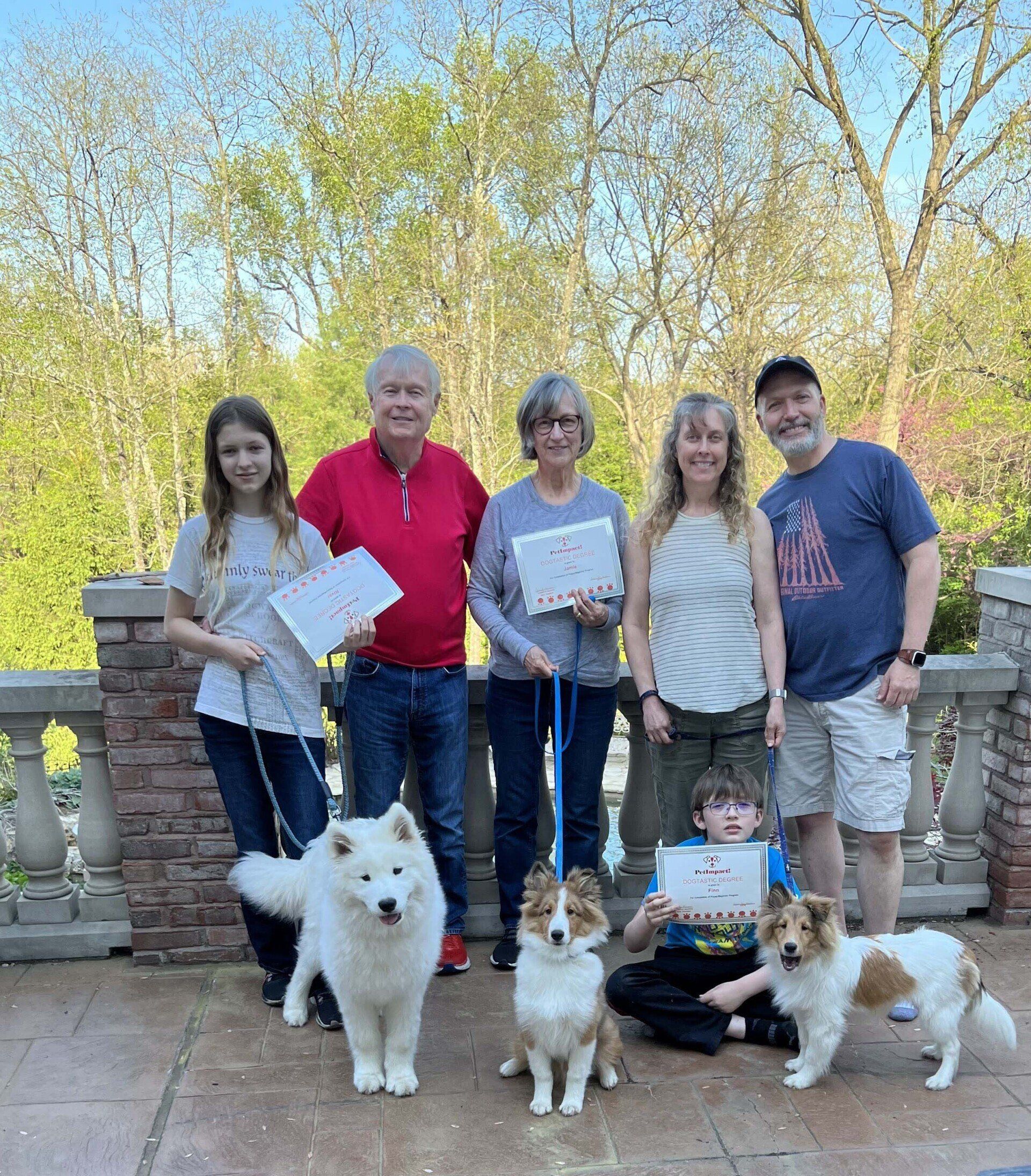 Group of people with dogs holding certificates outdoors.