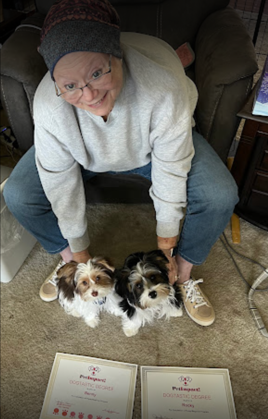 Woman seated with two small dogs on the floor. The dogs are by their award certificates.