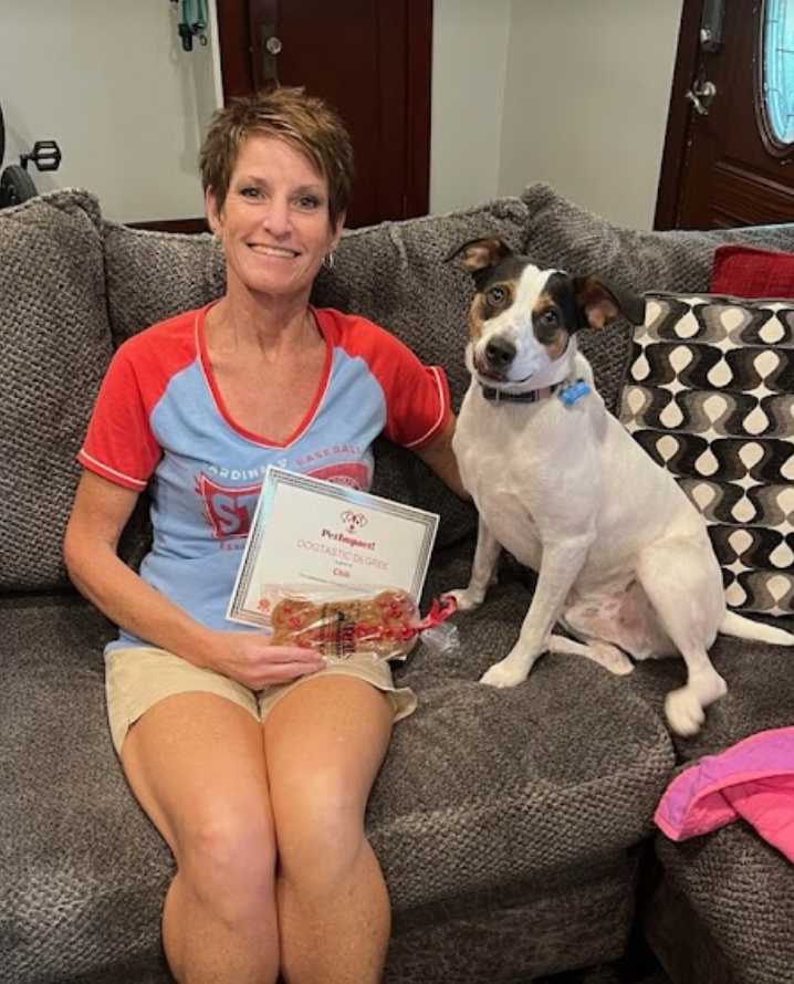 Woman and dog sitting on a gray couch, woman holding a certificate.