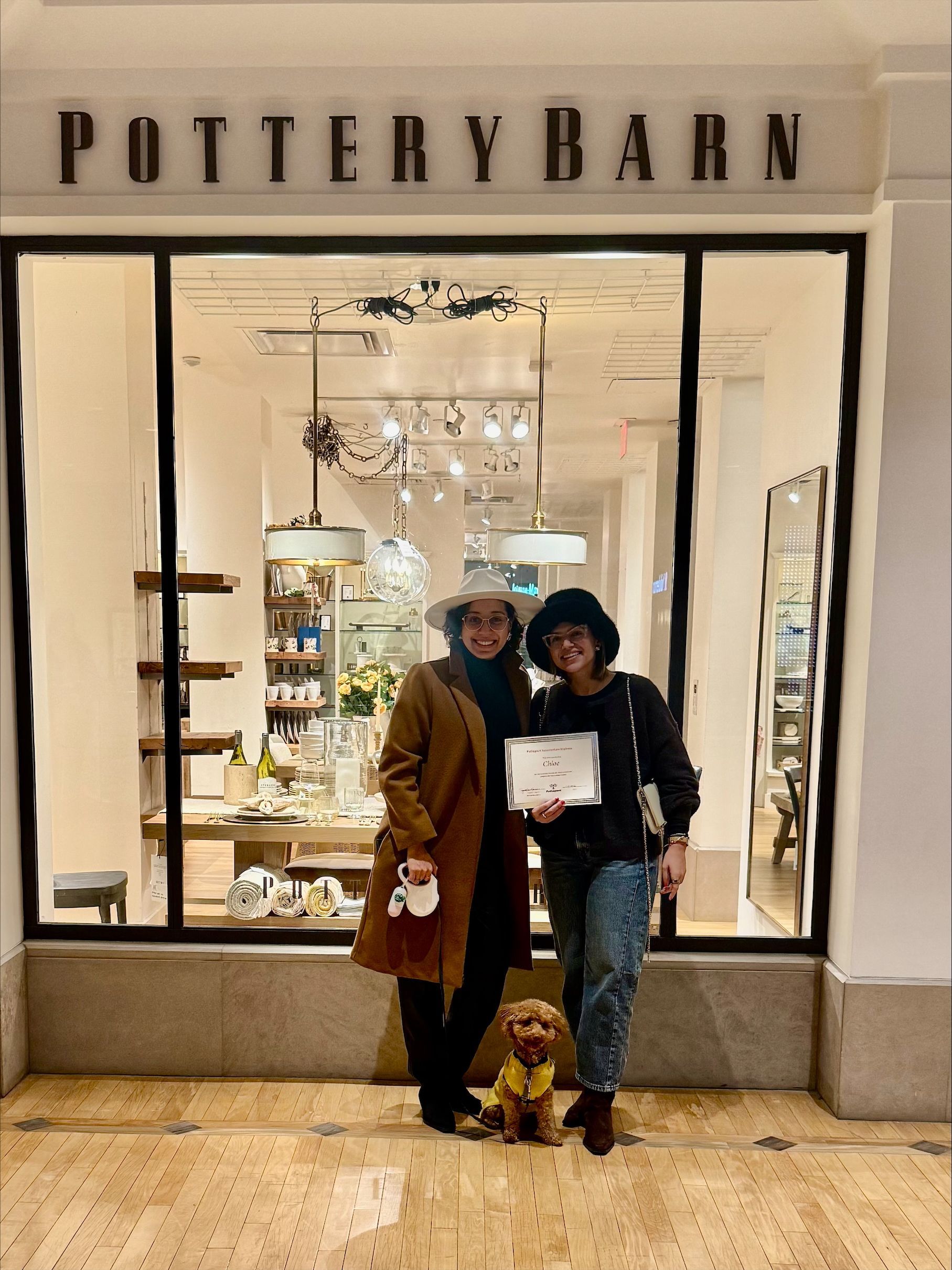Two people standing outside Pottery Barn storefront with a small dog between them