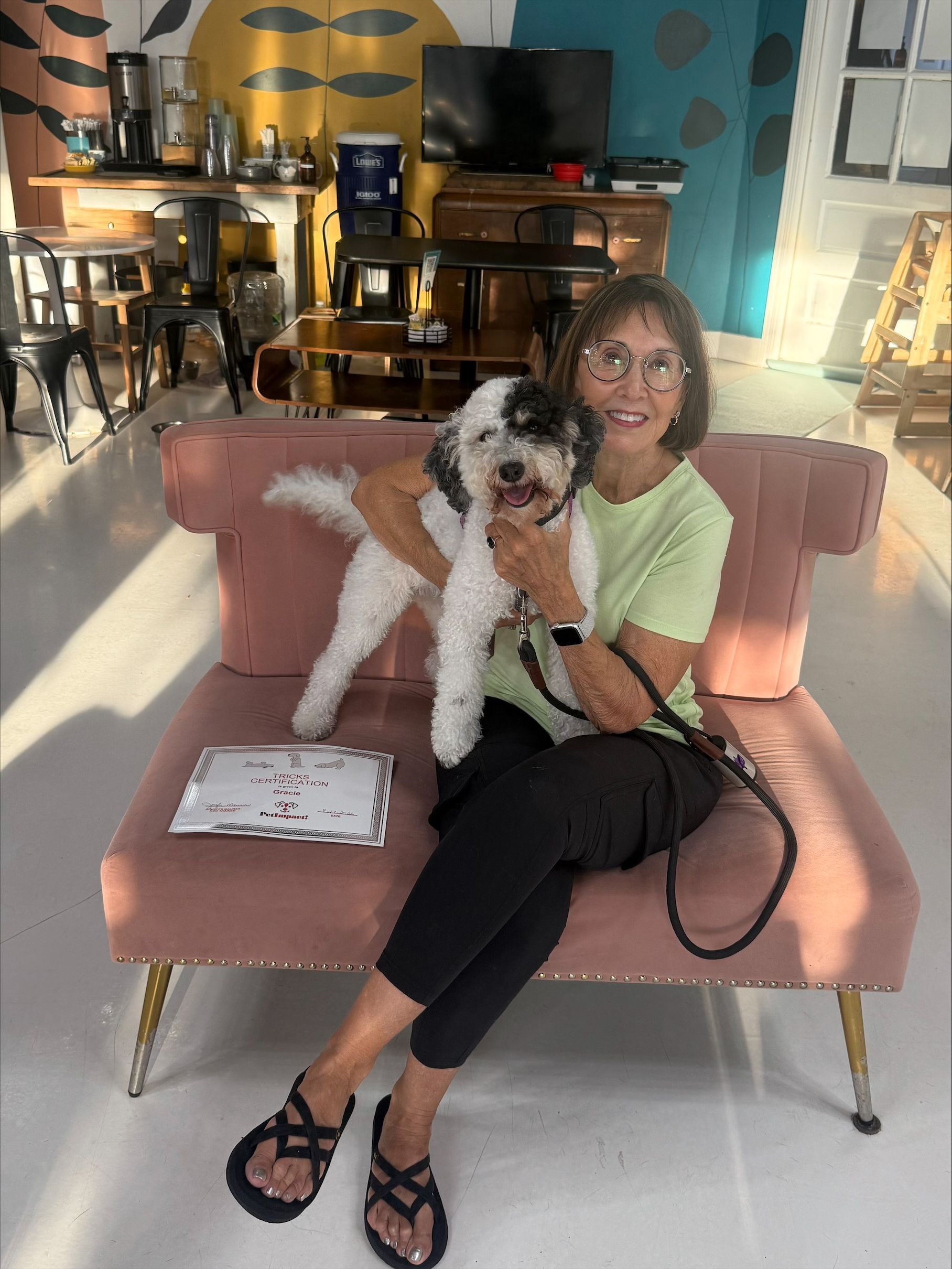 Woman sits on a pink couch holding a black-and-white dog in a bright living room.
