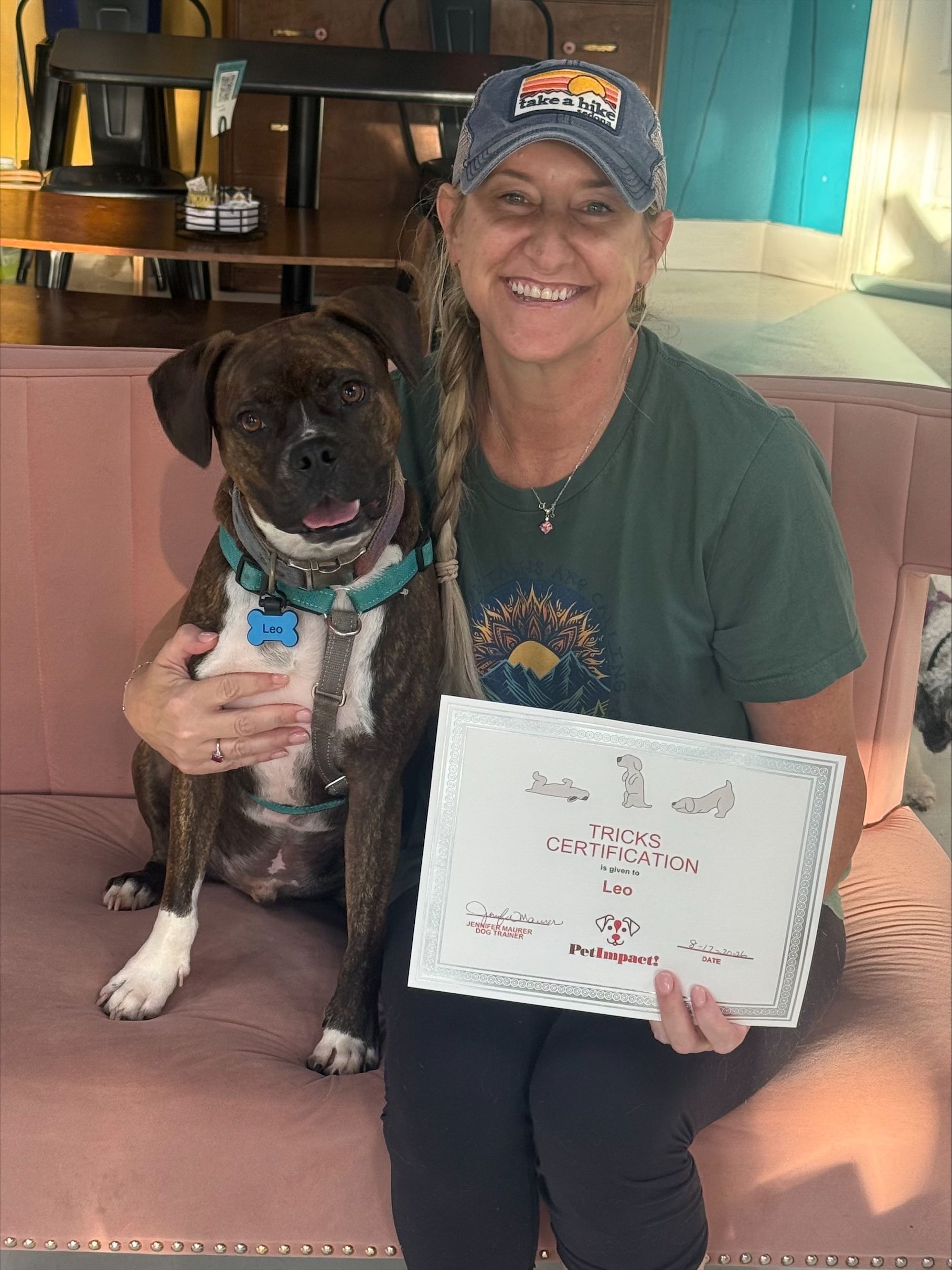 Woman smiling with a black dog, holding a handwritten sign indoors on a couch.