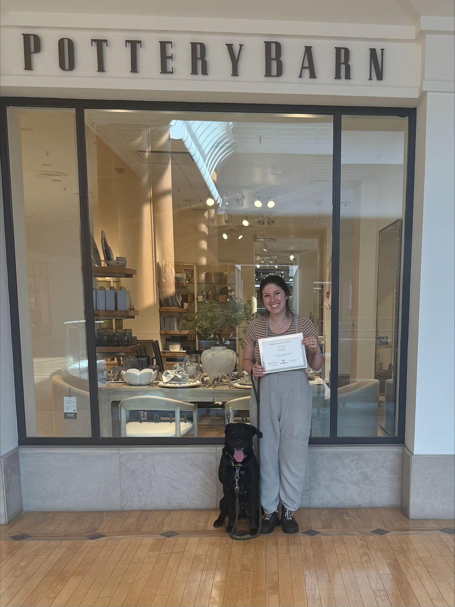 A woman holding a certificate with the dog next to her.
