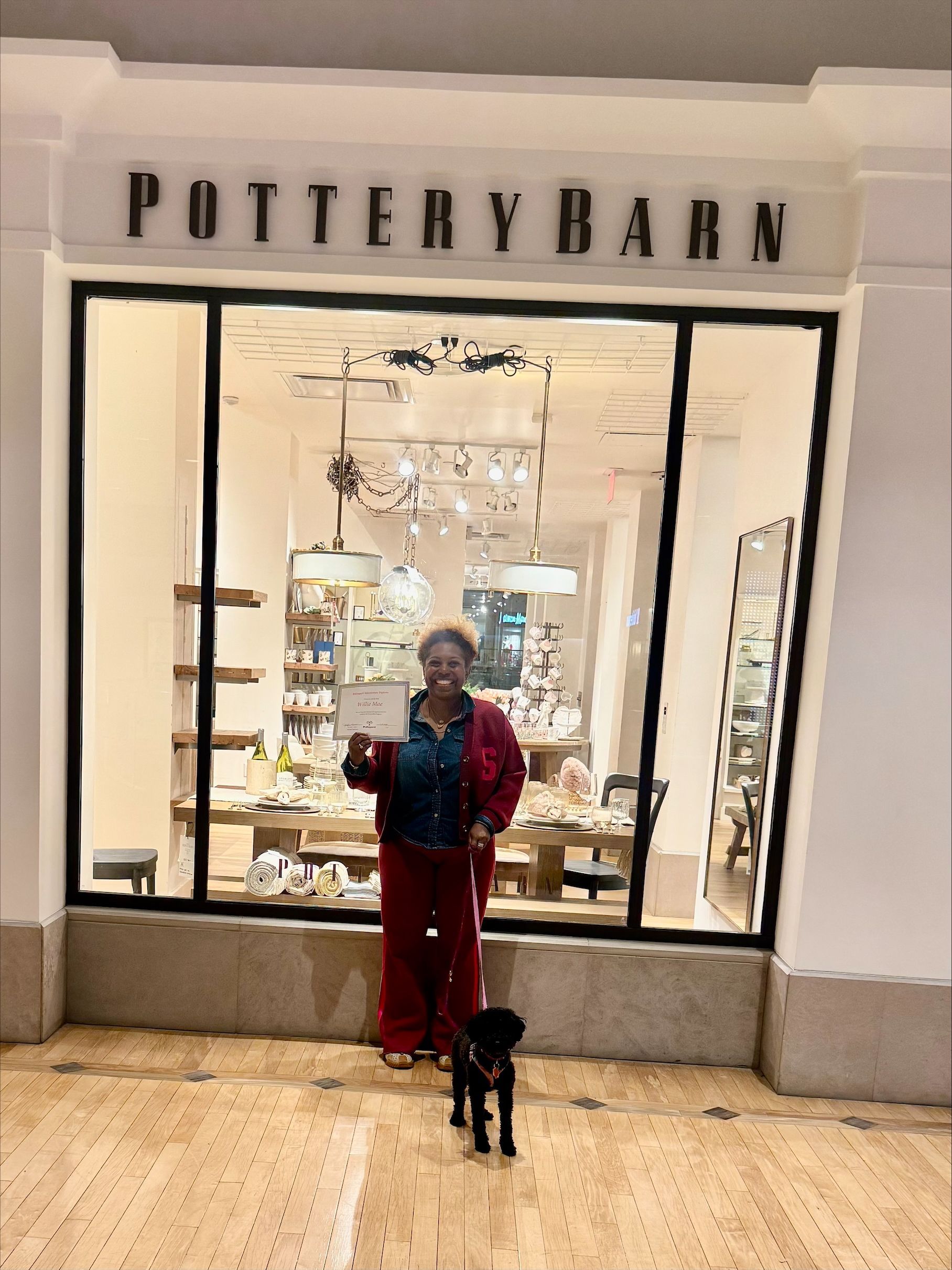 Person standing with a small black dog outside the Pottery Barn store window display