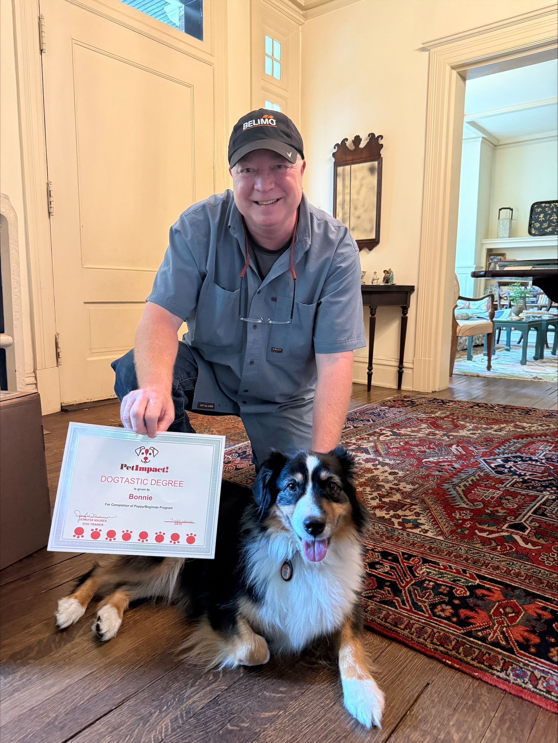 Man holding a sign beside a black-and-white dog in a bright living room