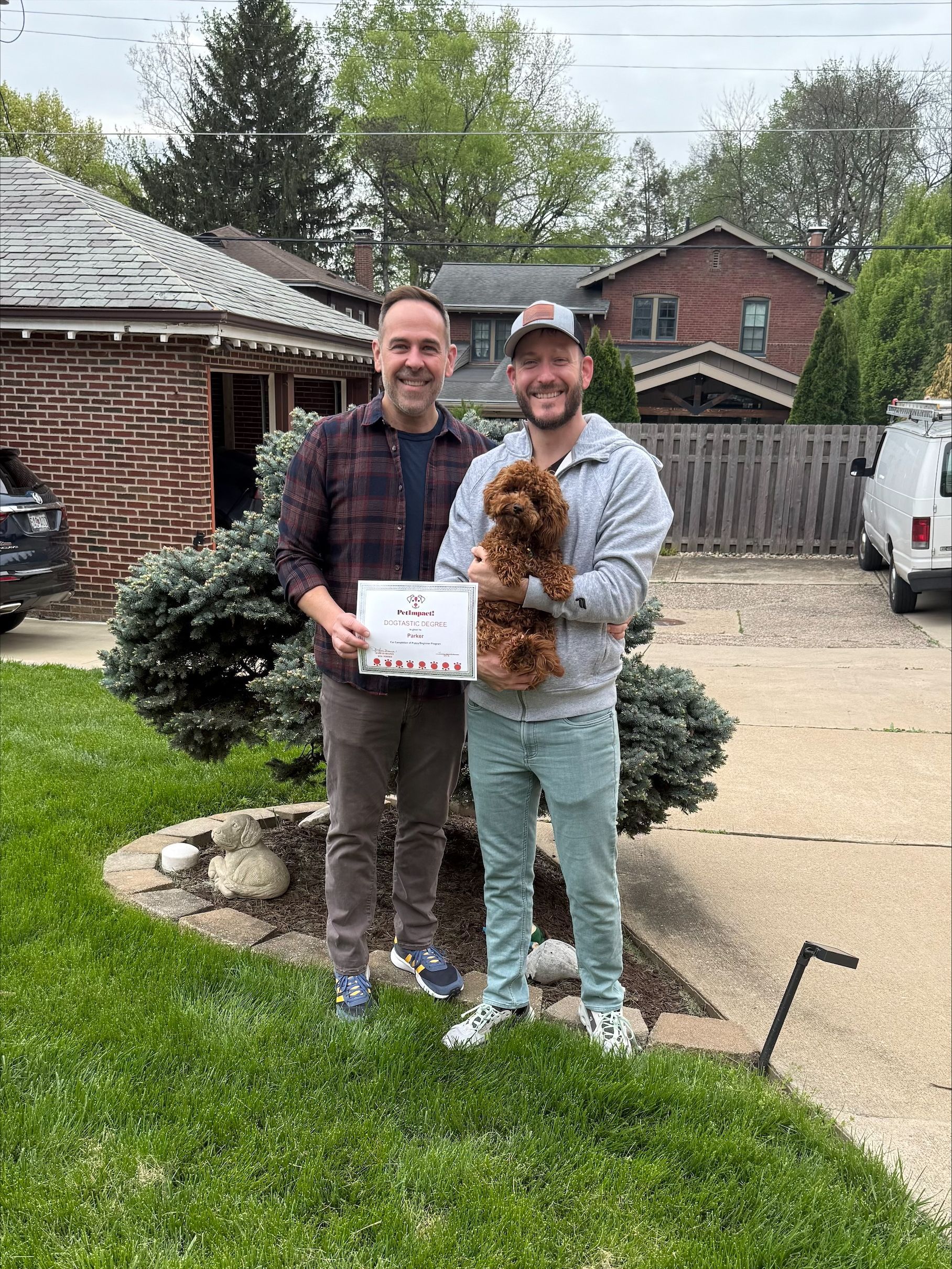 Two people standing and holding a dog and certificate.