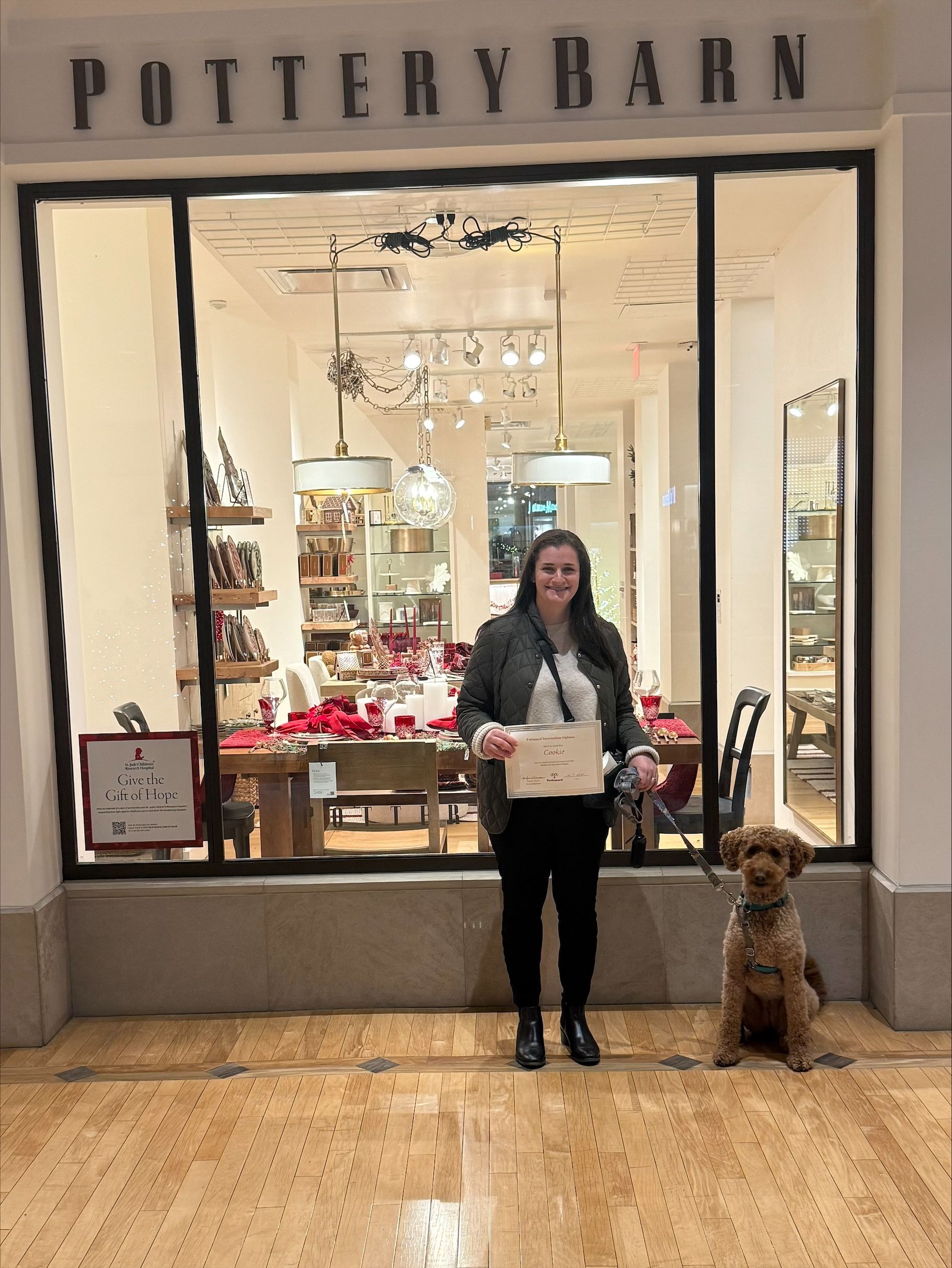 Woman posing outside a Pottery Barn store with a dog beside her.