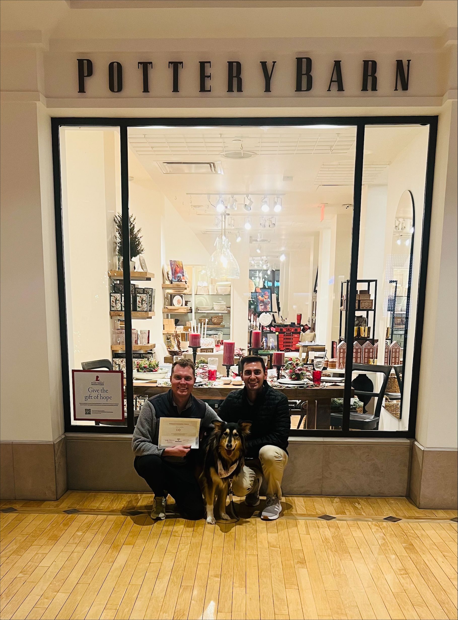 Two men and a dog are standing in front of a pottery barn store.