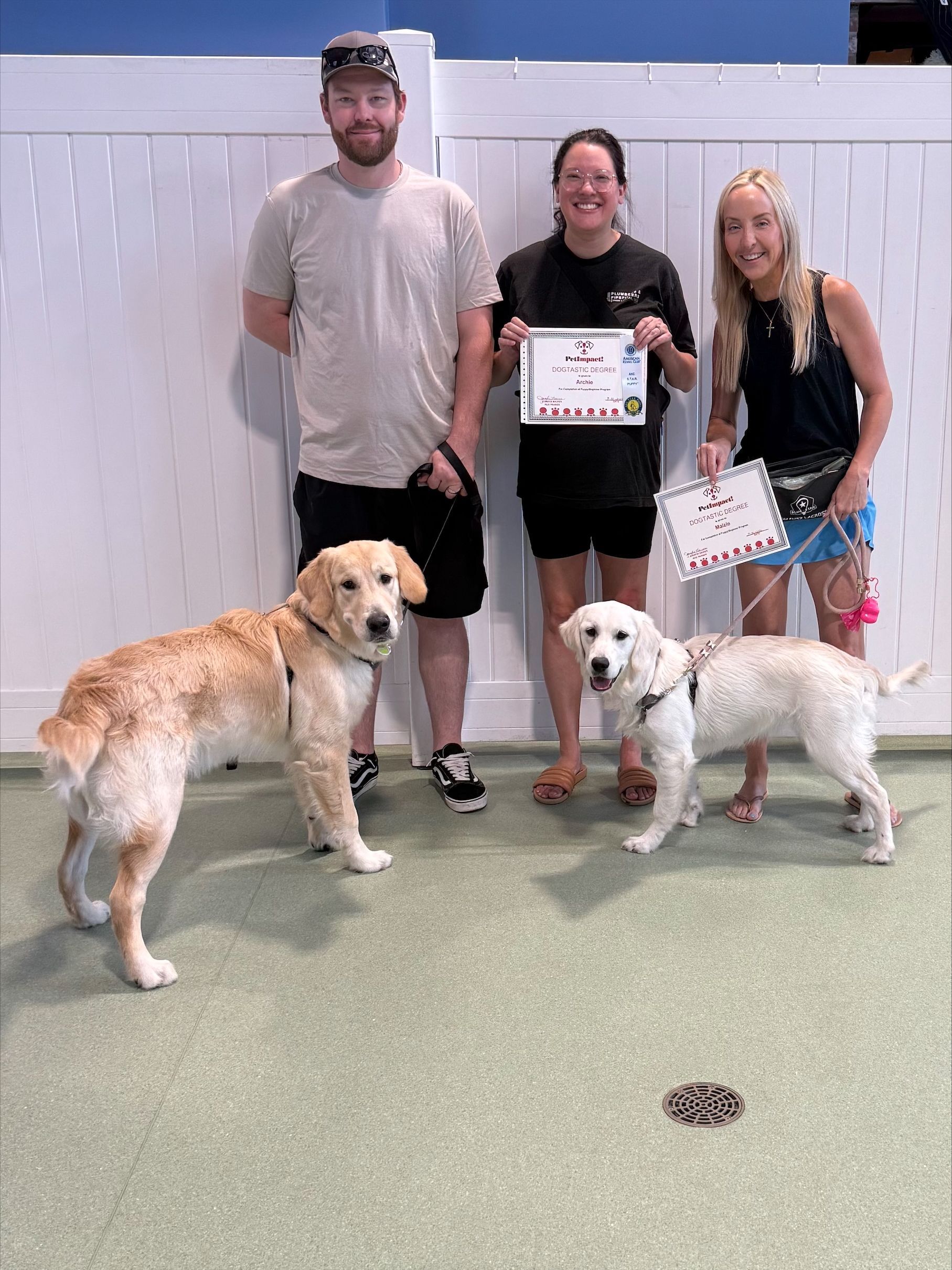 Three people with certificates posing indoors with three dogs, including a golden retriever and two small white dogs.