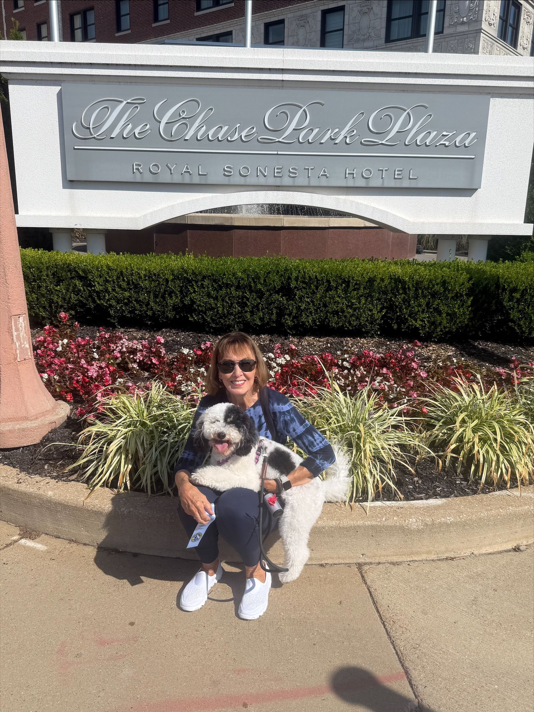 Woman kneeling with two dogs in front of The Chase Park Plaza hotel sign.