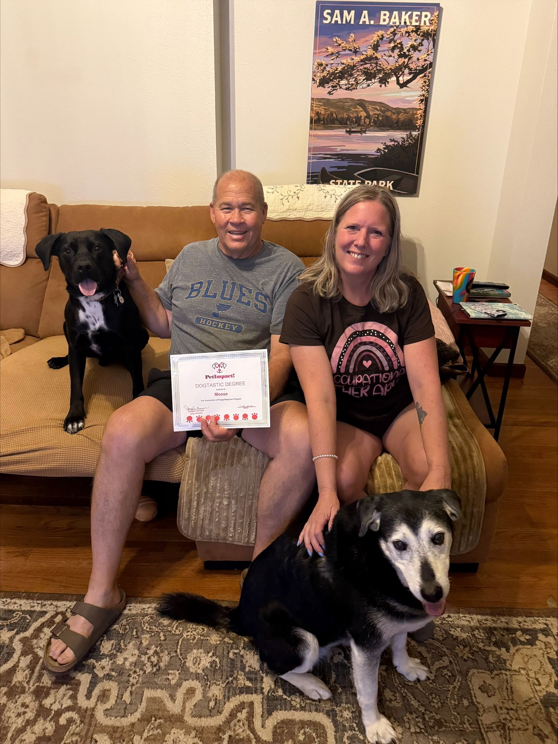 Two people holding a certificate with two dogs in a living room.