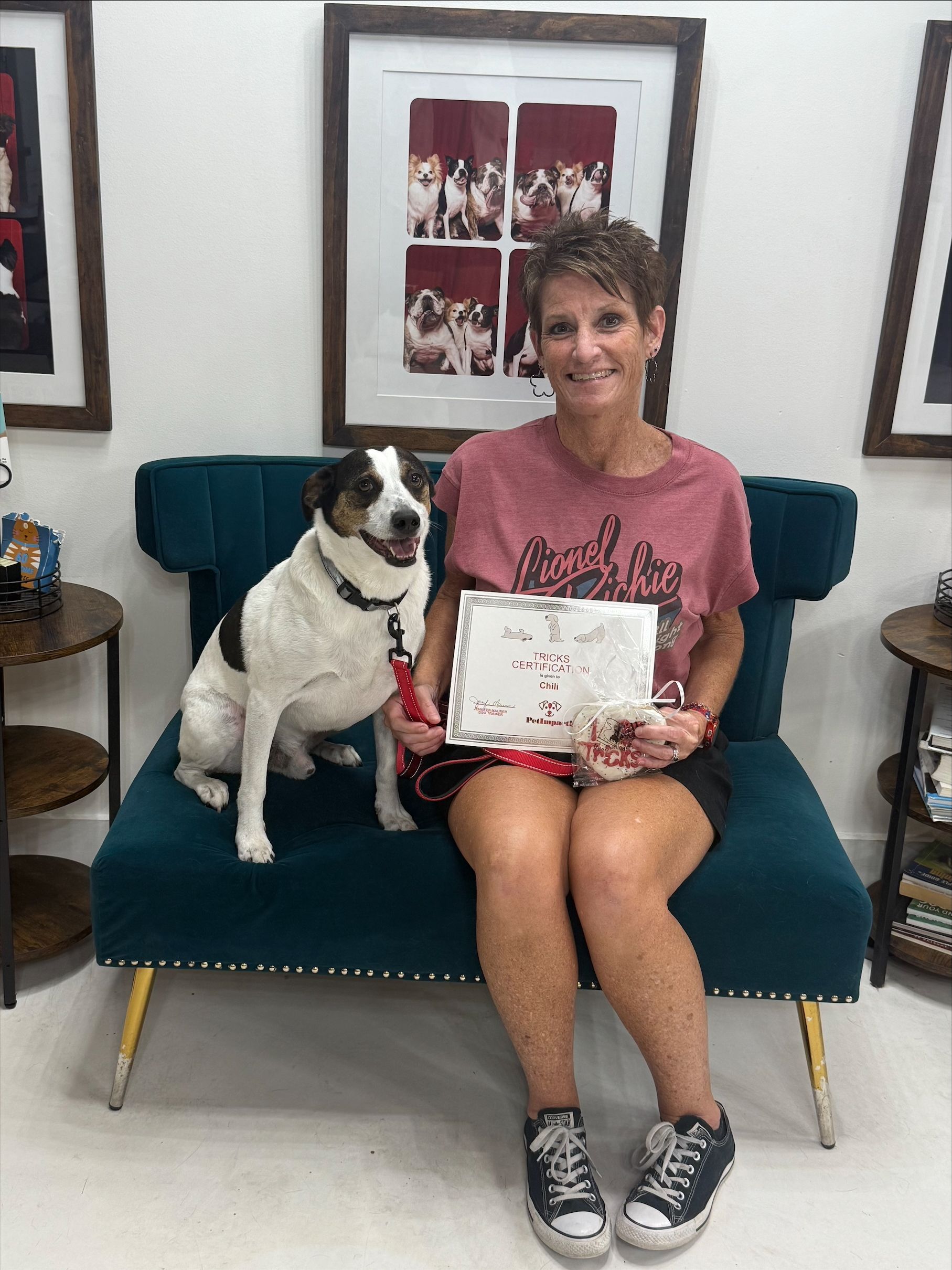 Woman sits on a teal couch holding a certificate with a black-and-white dog beside her.