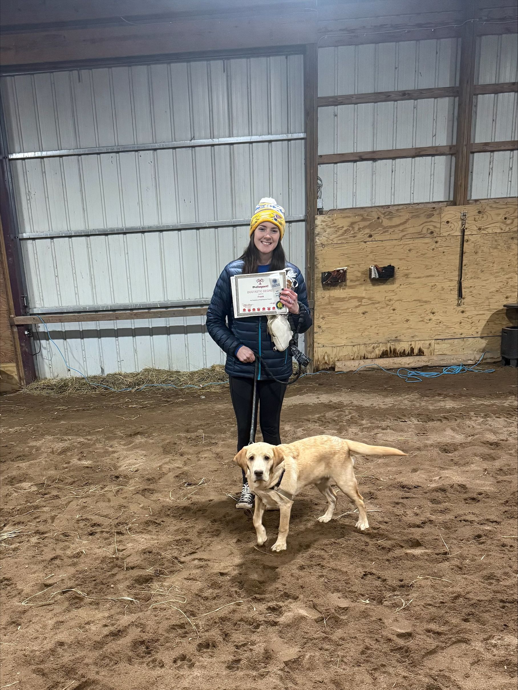 Person standing indoors with a golden dog in a barn-like space, holding a sign.