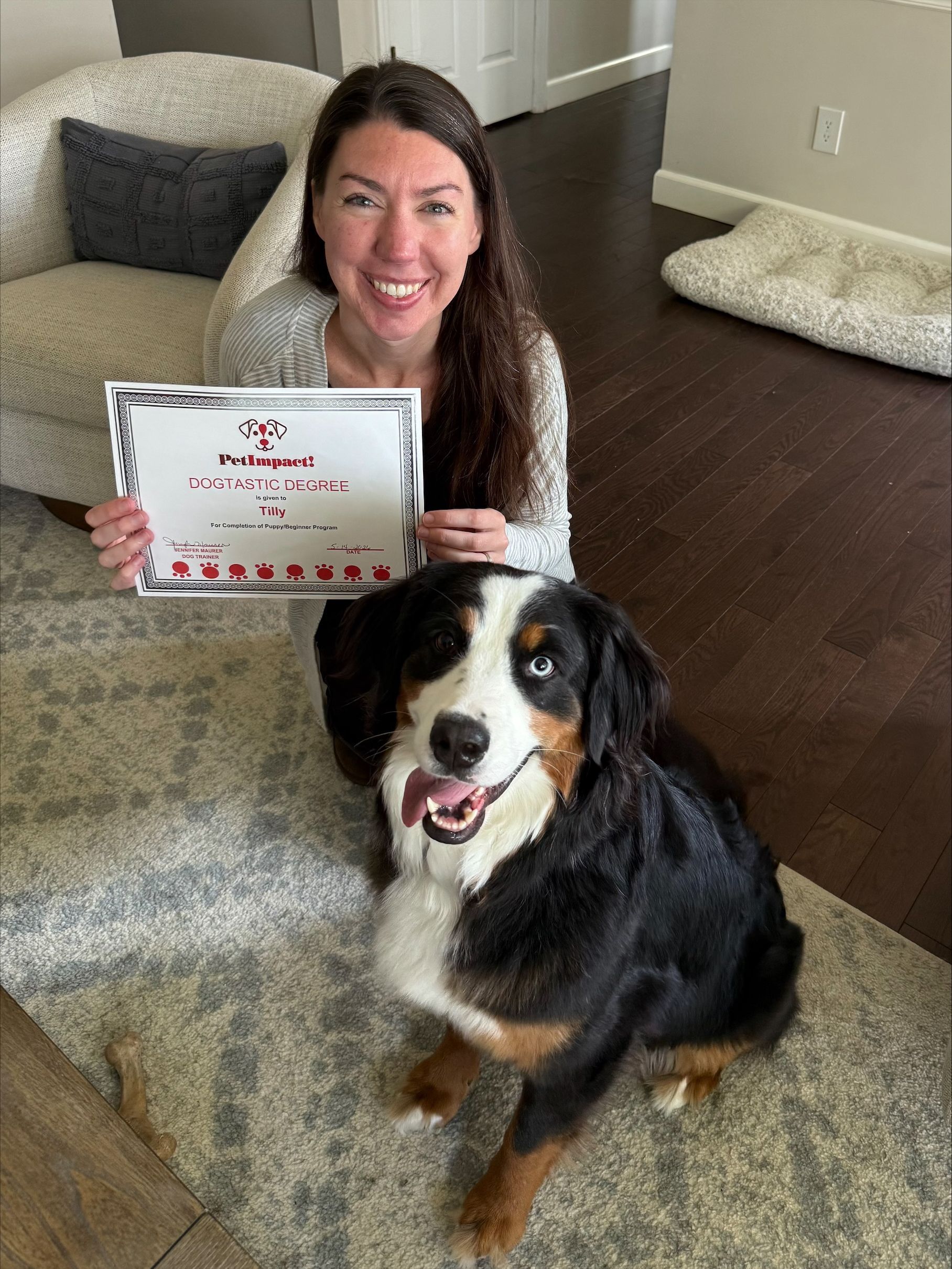 Smiling woman holding a sign beside a black, white, and brown dog on a dark hardwood floor