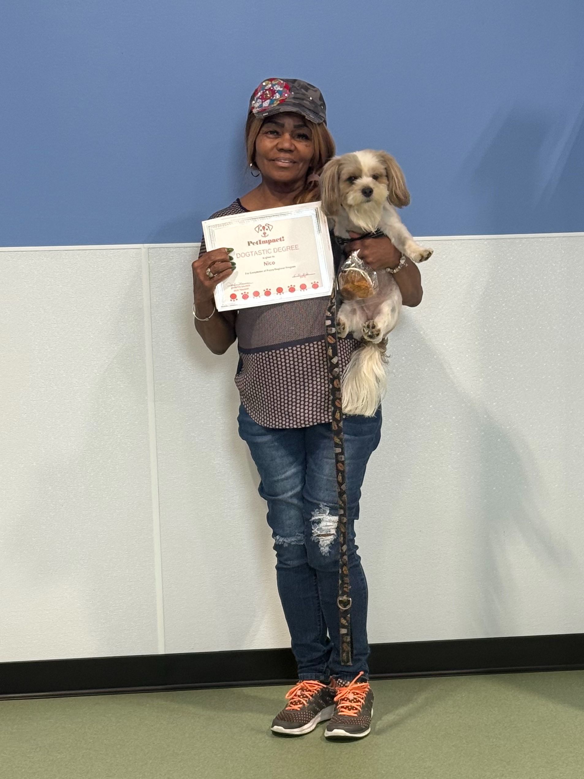 Person holding a small dog and a certificate, standing against a blue and white wall.