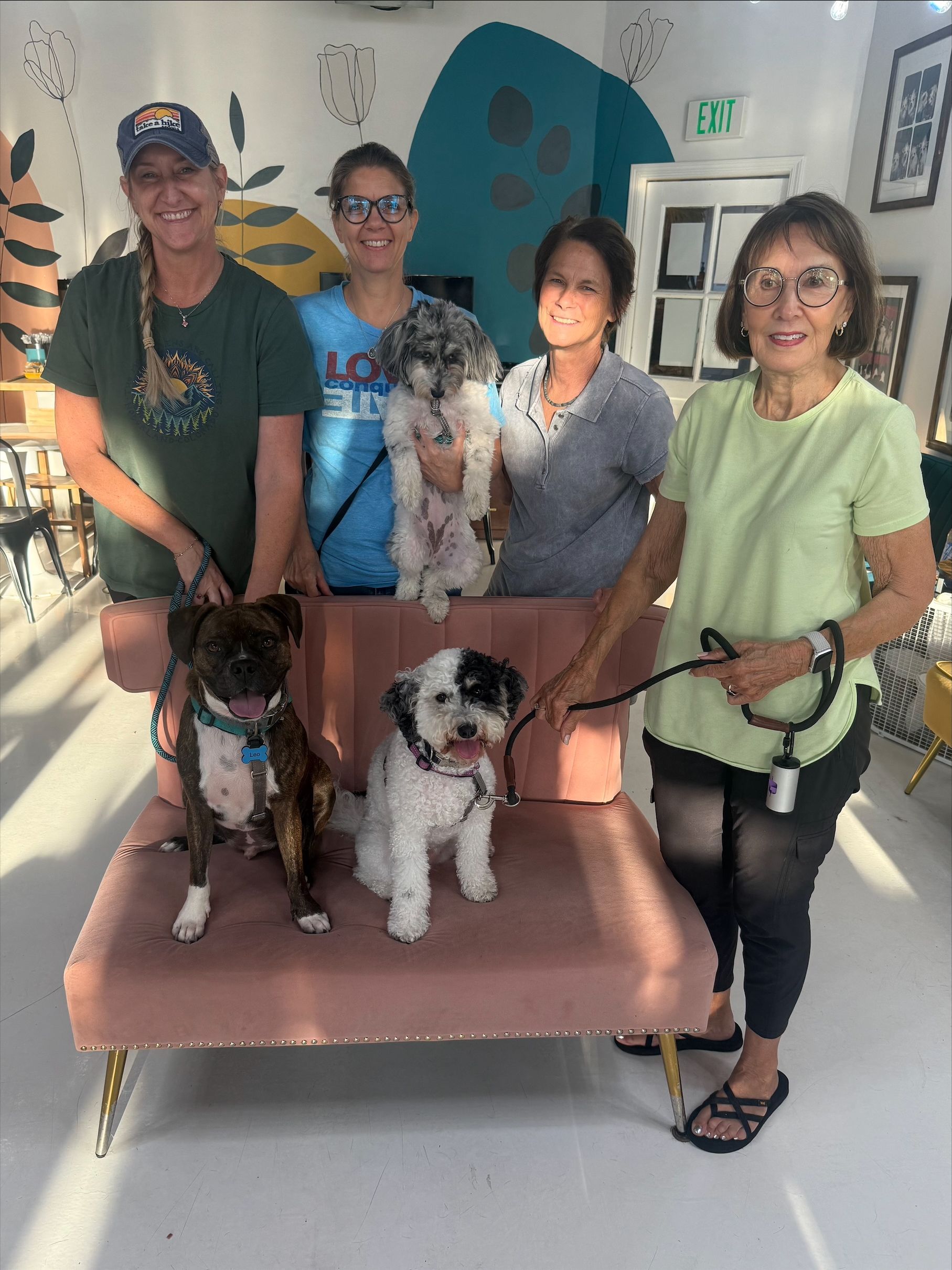 Five people pose with three dogs on a couch in a bright room.