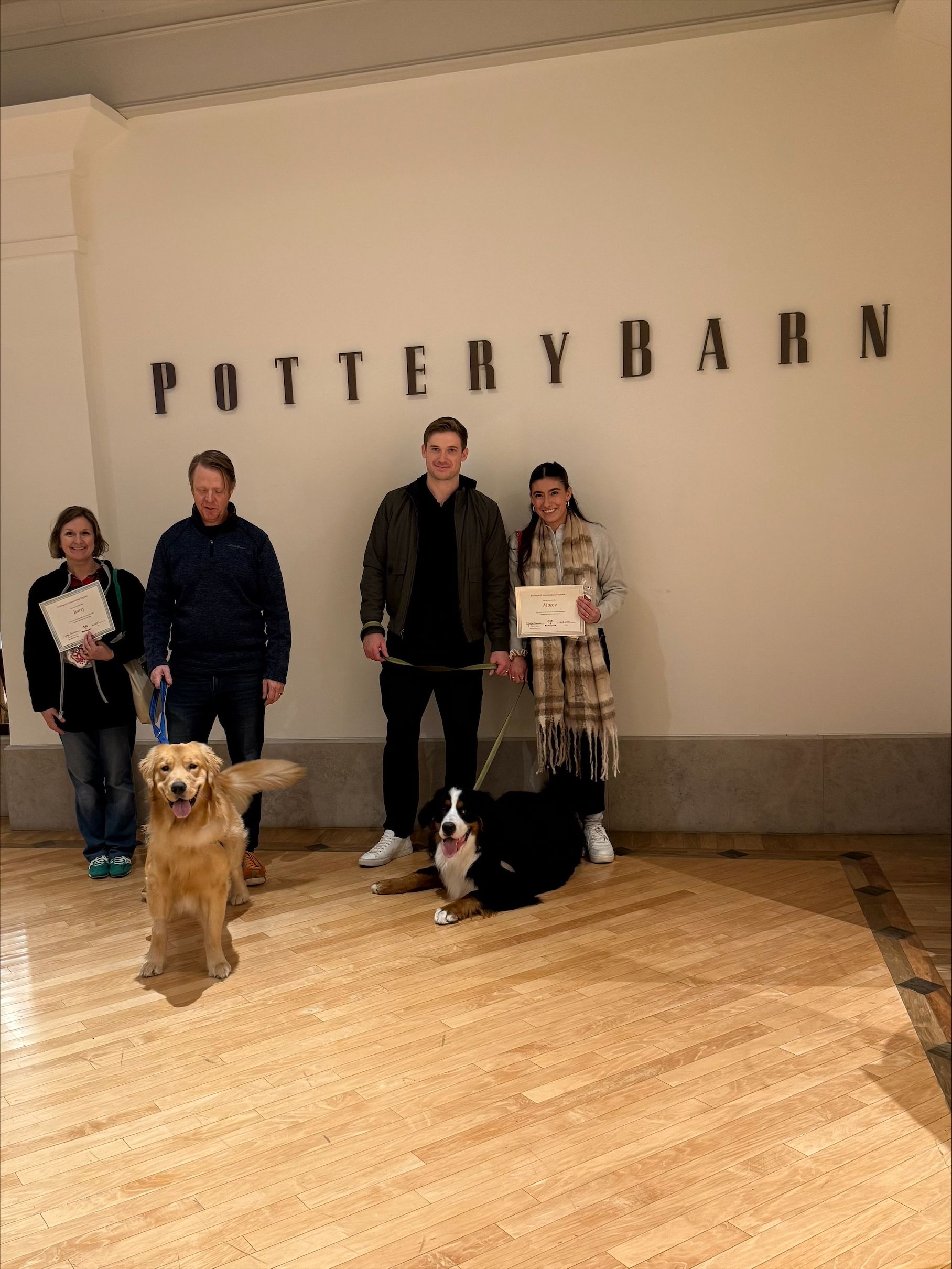People and dogs posing in front of a Pottery Barn store sign.