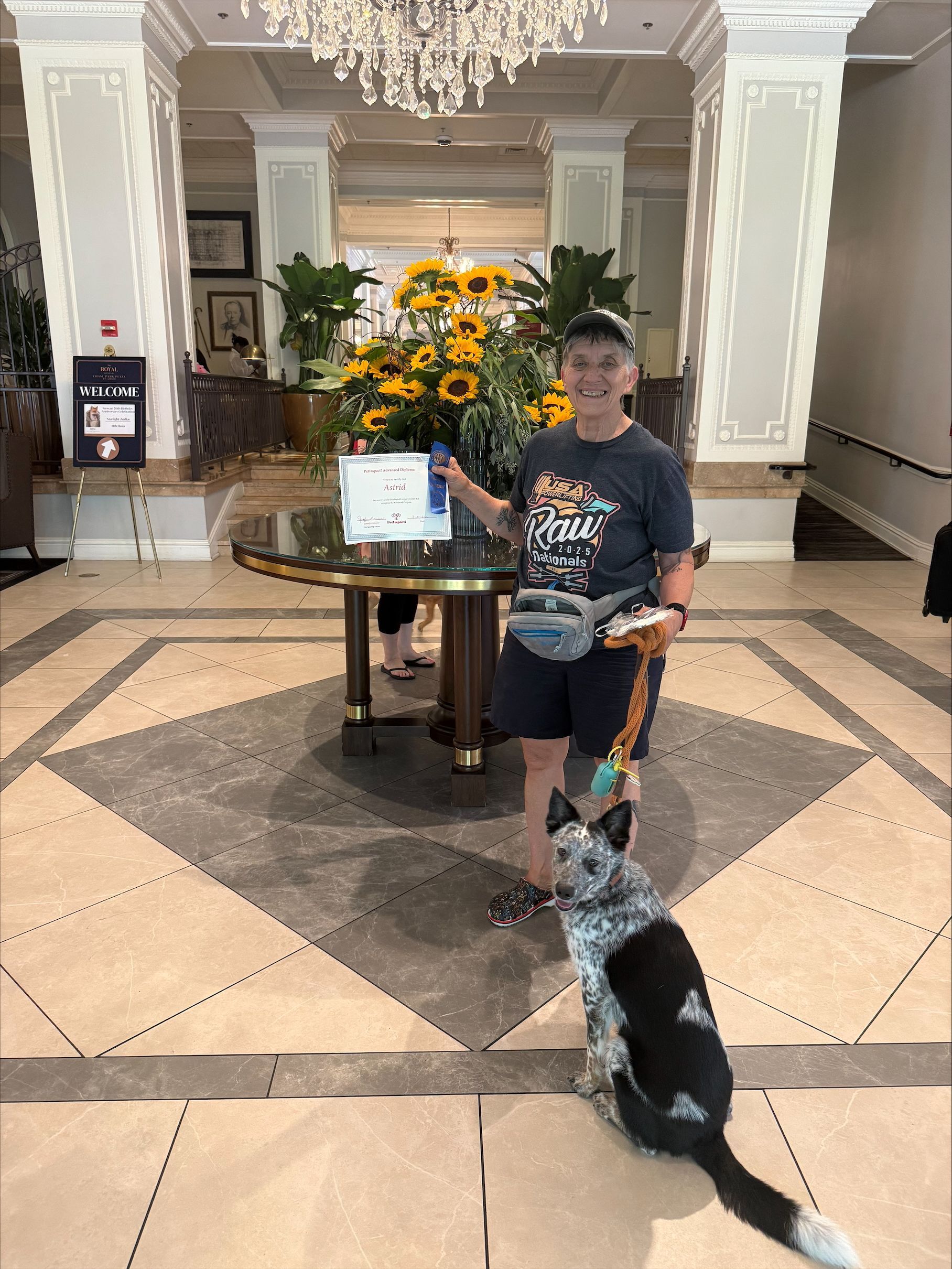 Person with a black-and-white dog in a grand hotel lobby beside a floral display