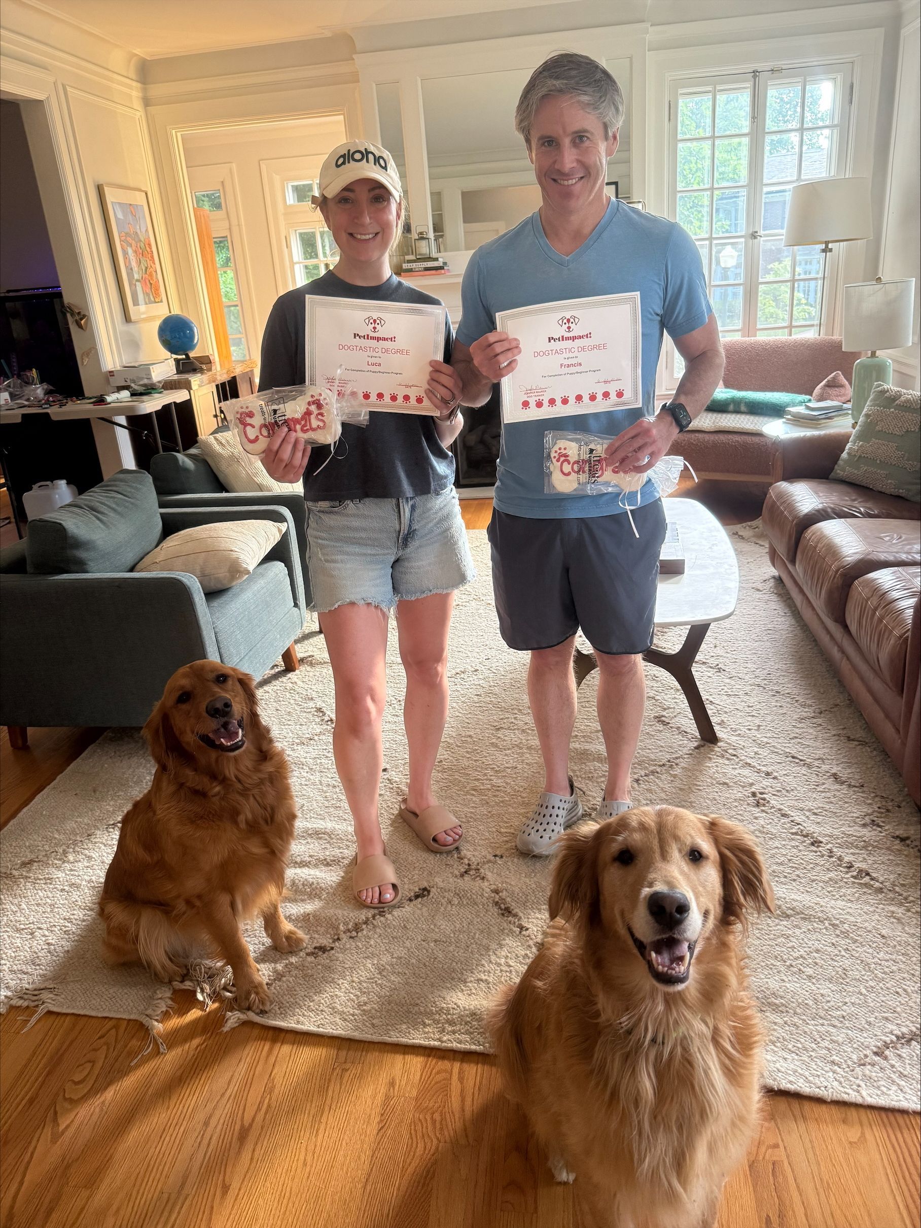 A couple holding 2 certificate together with two golden retriever dogs.