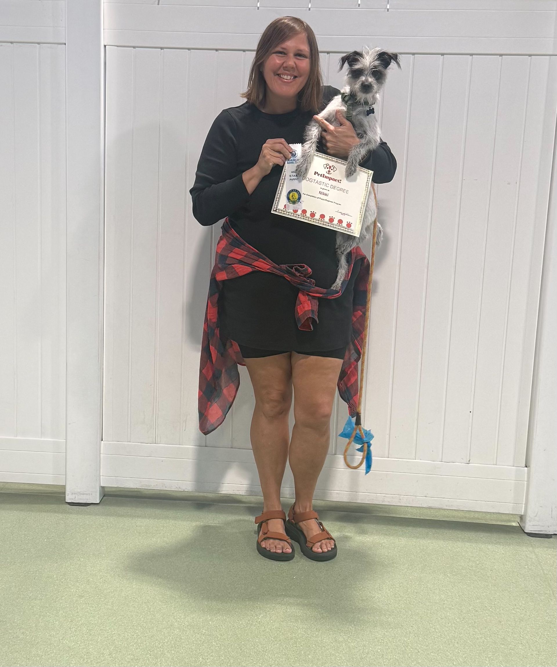 Woman holding a small black-and-white dog and a certificate in front of a white fence
