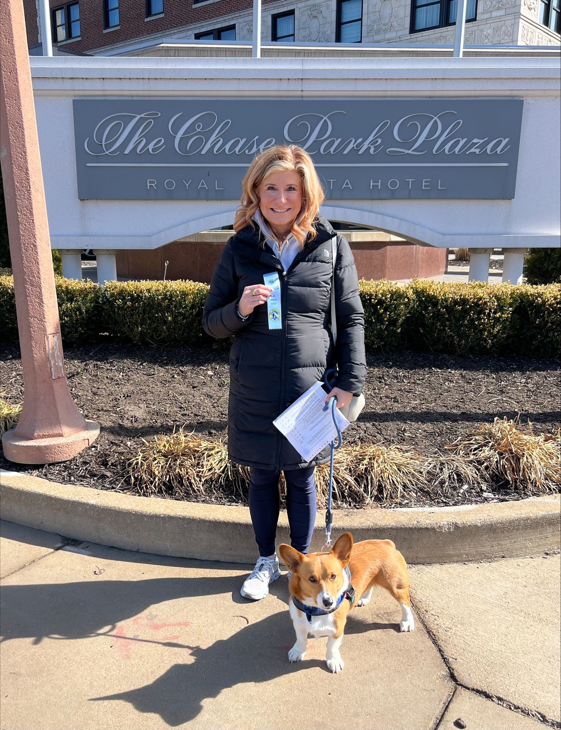 A woman is standing next to a dog on a leash in front of a hotel sign.