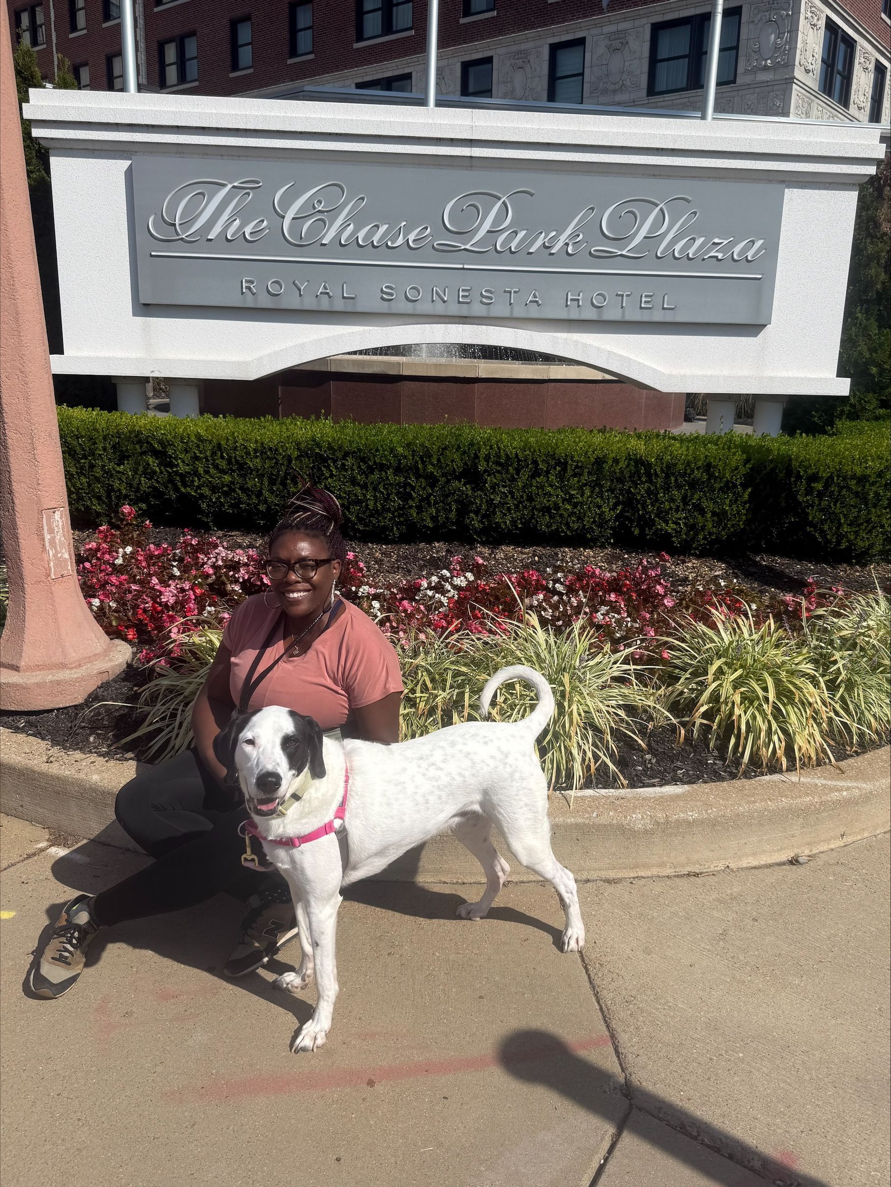 Woman and white dog with black spots in front of The Chase Park Plaza hotel sign.