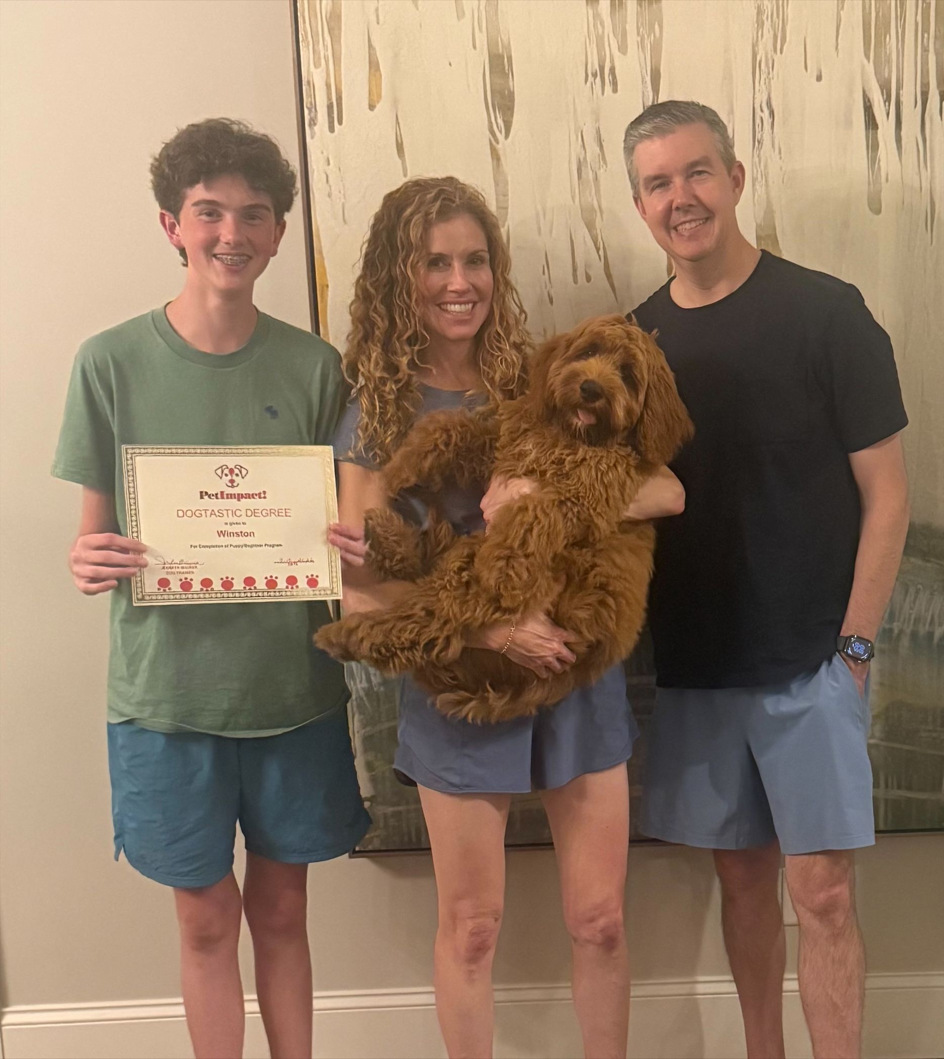 Three people indoors, one holding a brown dog and another holding a certificate, posing and smiling.