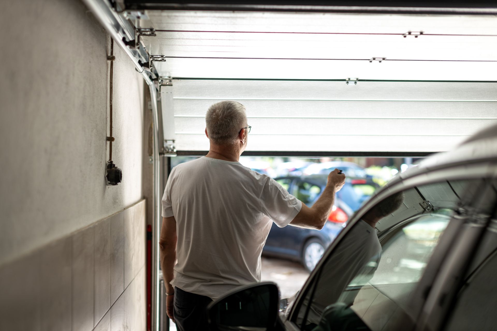 Man in white t-shirt opening garage door, next to a car.