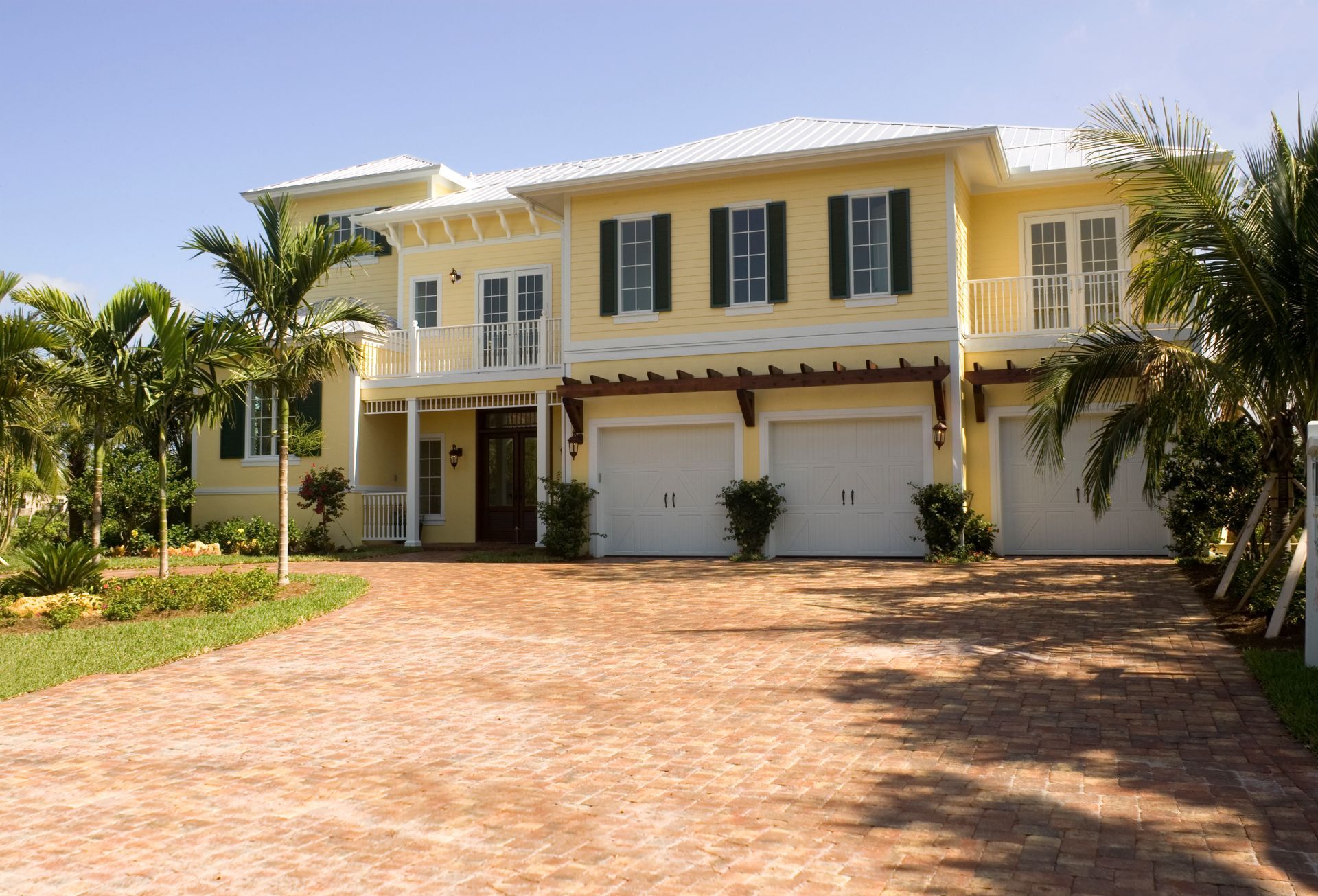 Yellow two-story house with white trim, green shutters, and a three-car garage; brick driveway.