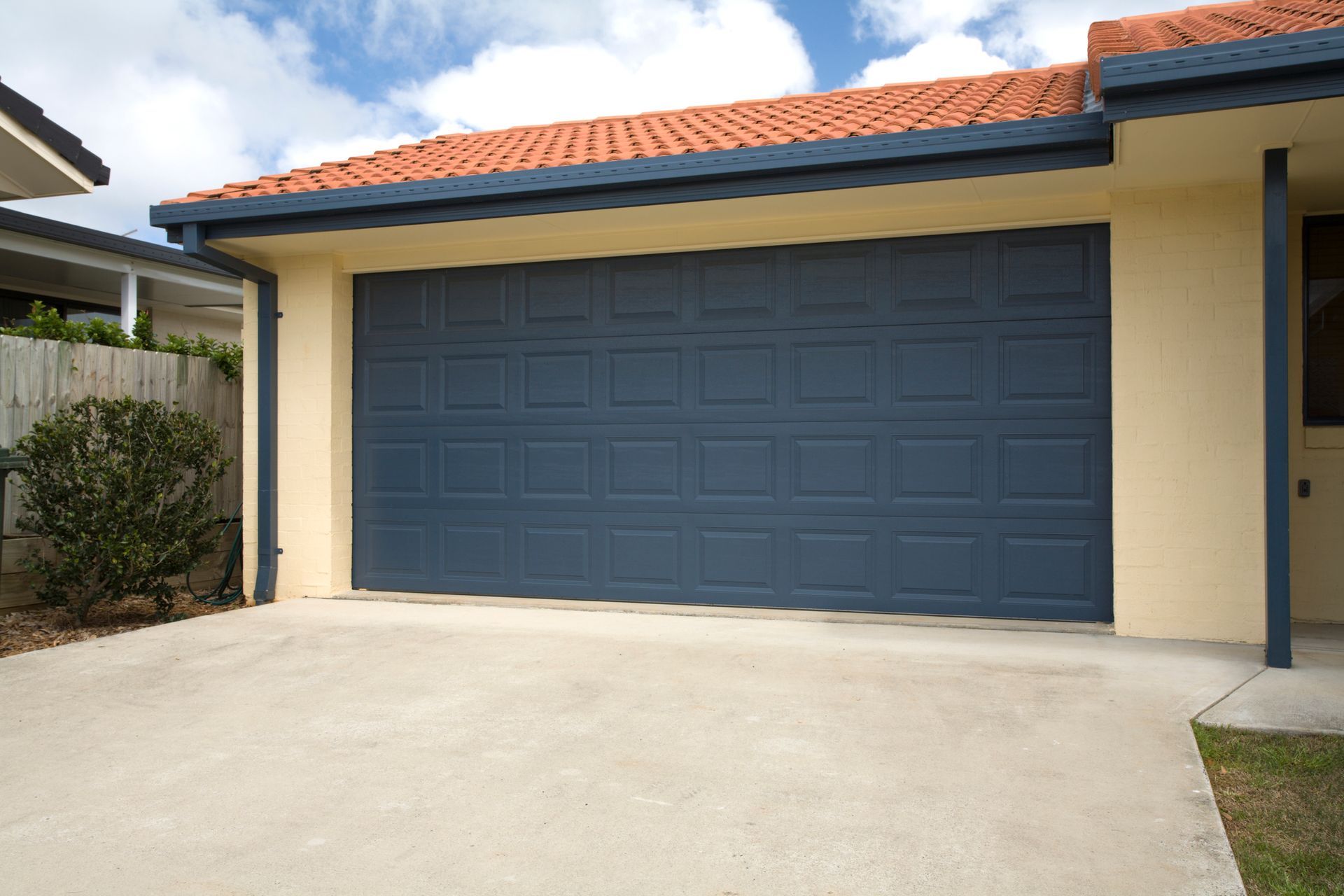 Blue garage door on a light tan house with an orange roof and concrete driveway.