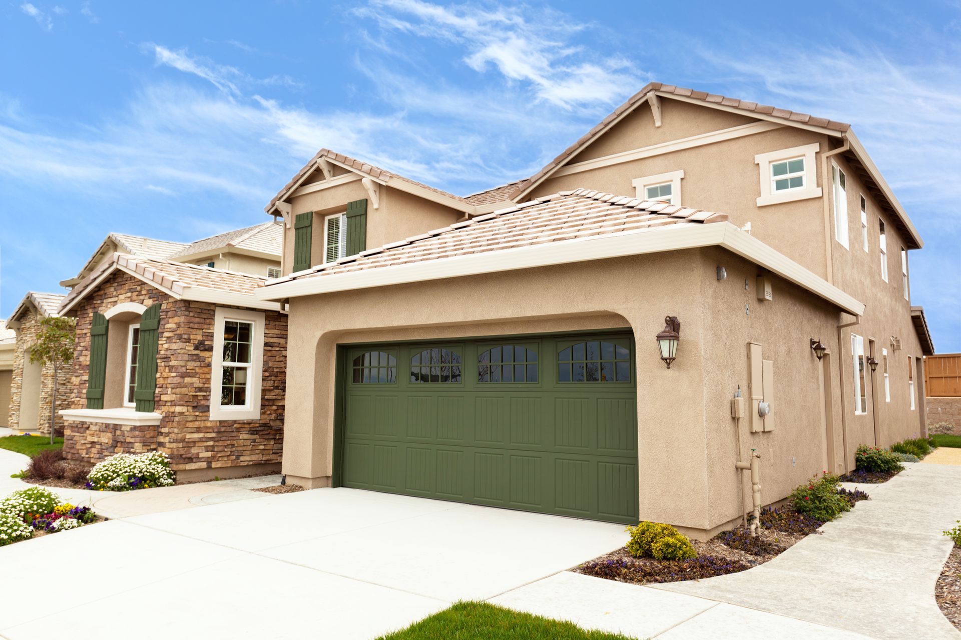 Beige two-story house with green garage door, brick accents, and blue sky.