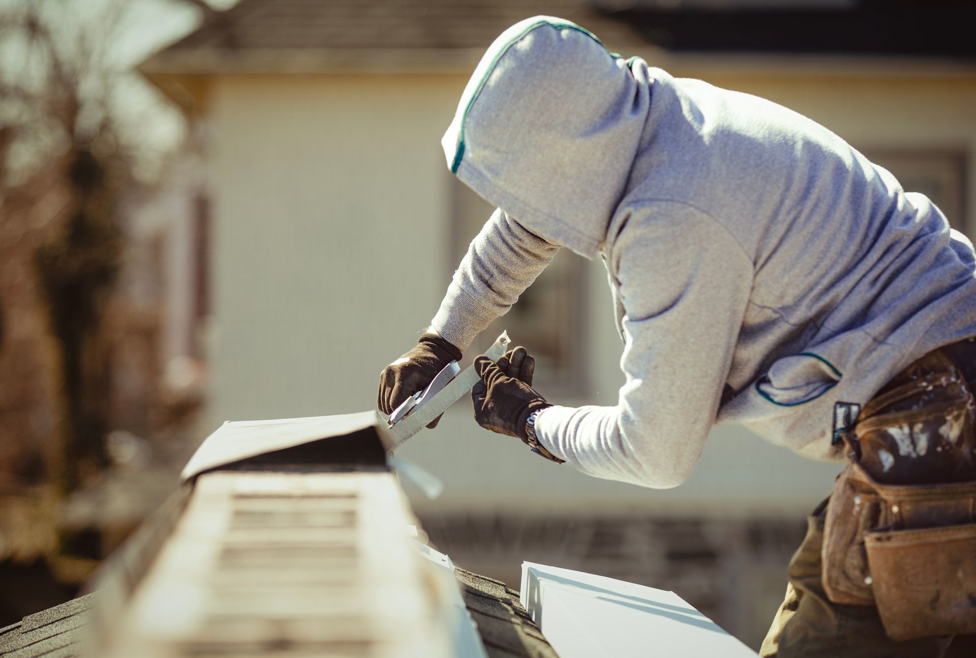 Worker in a hooded sweatshirt sealing a rooftop seam with a tool.