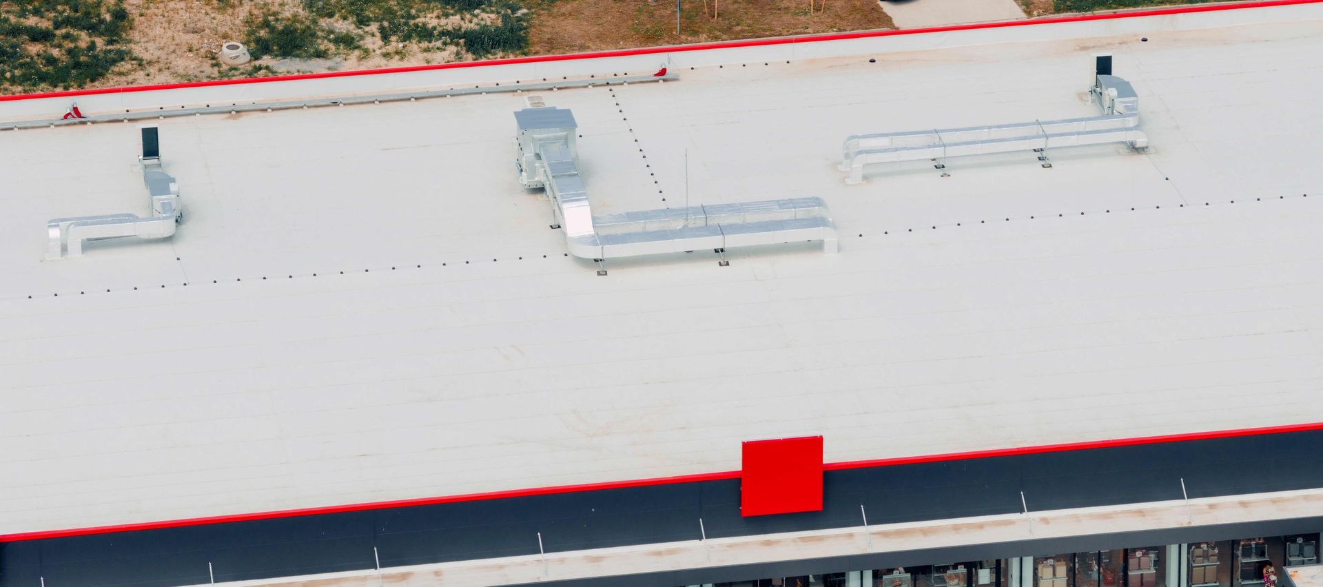 Aerial view of a white building roof with vents, skylights, and a red section near the edge.